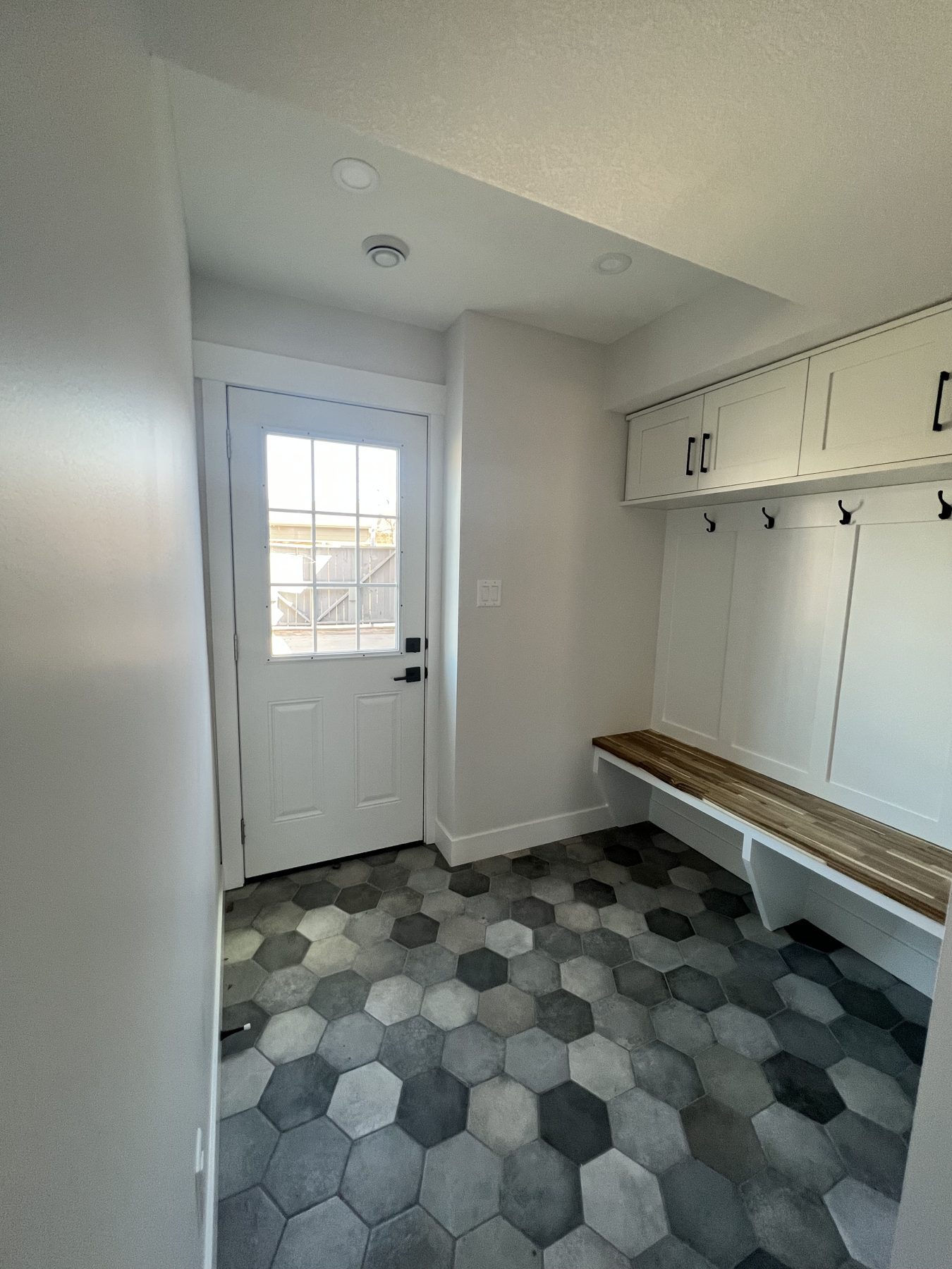 Mudroom entryway with hex tile, bench, and wall cabinets — 720 Lake Twintree Crescent SE, Calgary
