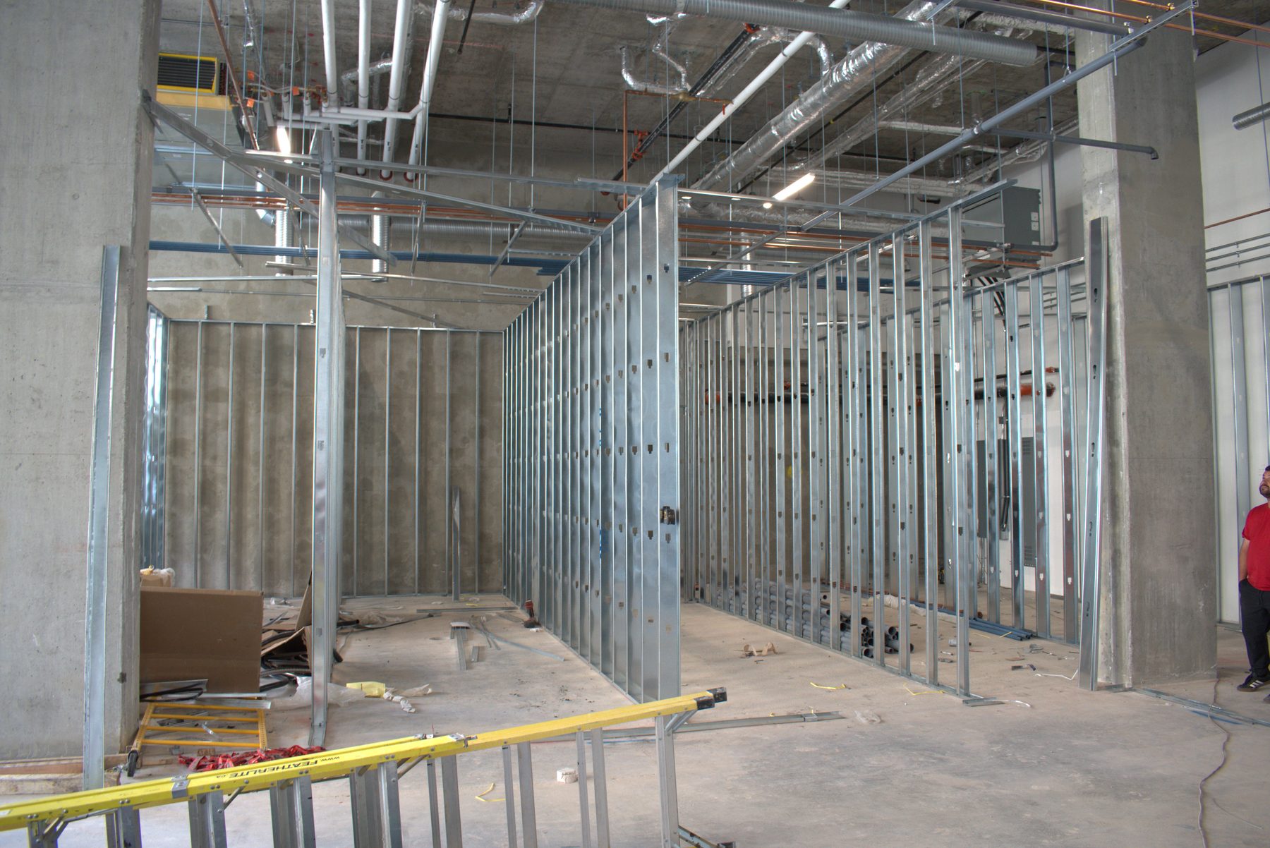 Metal stud framing forms walls in a concrete room with exposed conduits and piping — Leela Spa (West District)