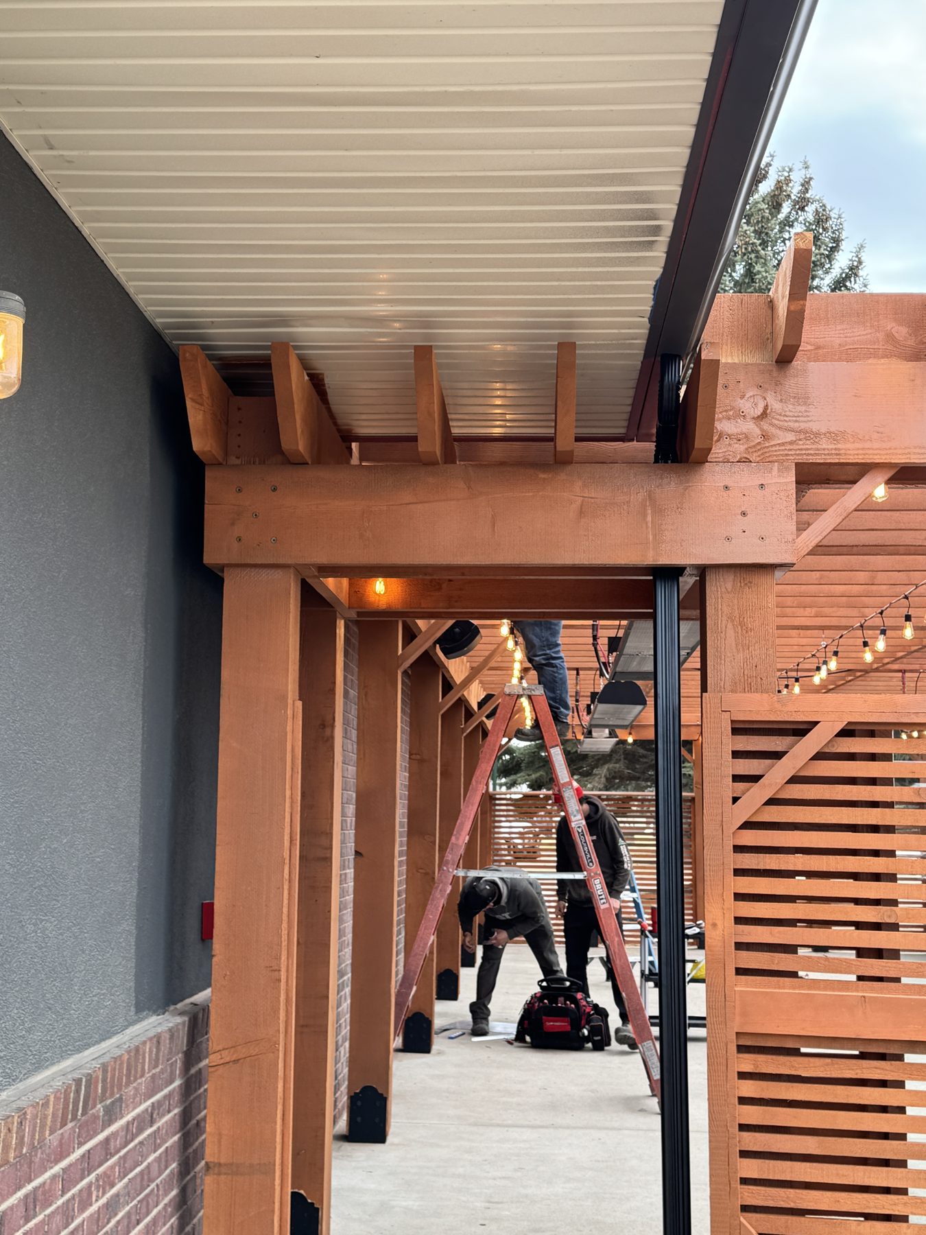 Workers install wooden pergola with metal roof over concrete patio — Blowers and Grafton (Medicine Hat)