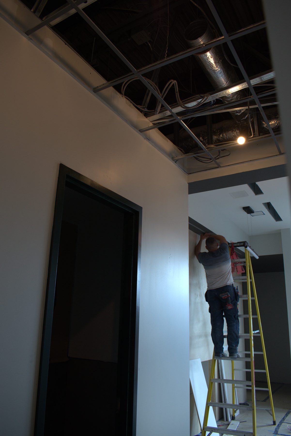 Worker on ladder installs ceiling grid and ductwork — ONE8T (West District)