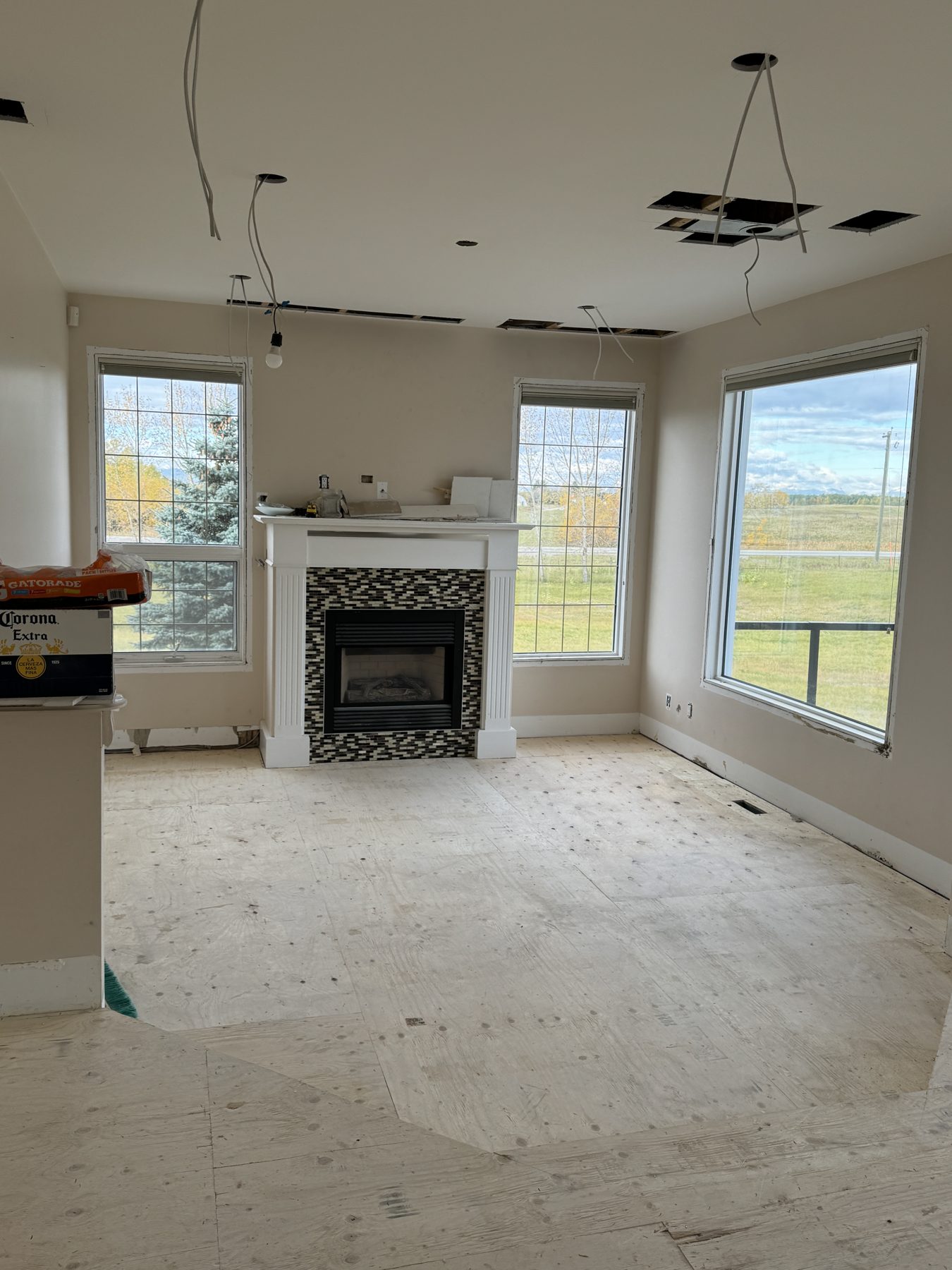 Fireplace renovation with exposed wires and plywood subfloor, windows and unfinished walls — 14 Lochend Drive, Cochrane