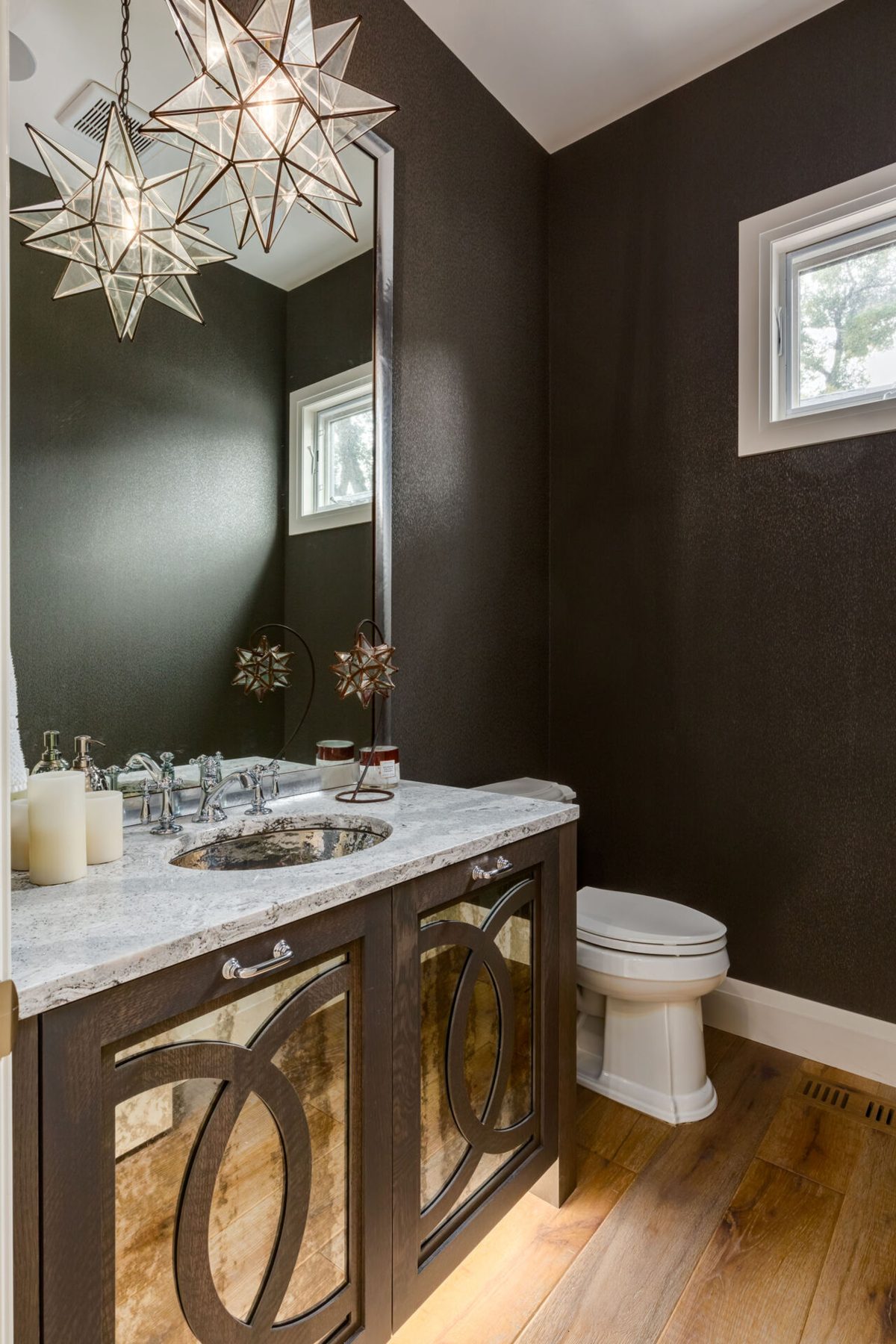 Powder room with dark textured walls, ornate vanity, and starburst chandeliers — Artista