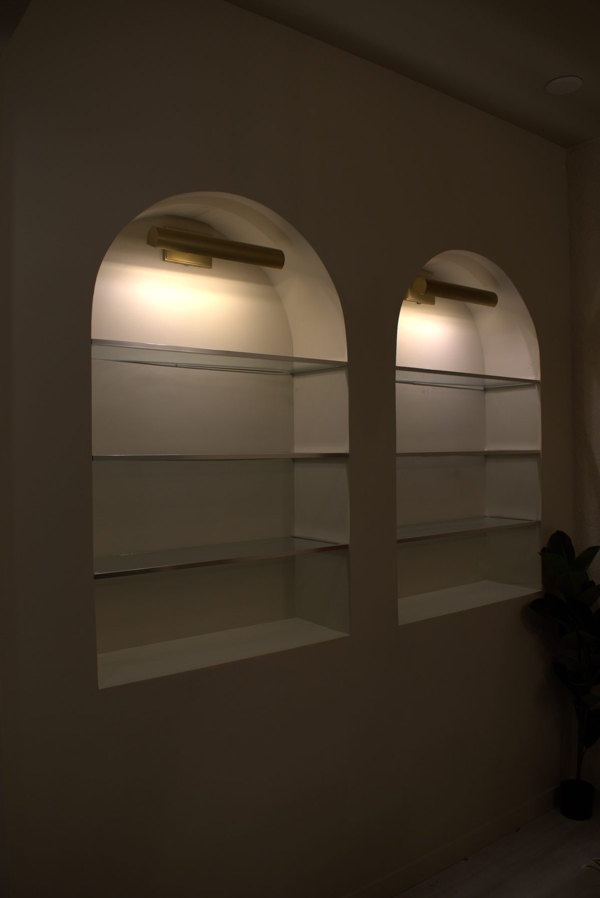 Arched alcoves with glass shelves and brass wall sconces are installed — Leela Spa (Bankers Hall)