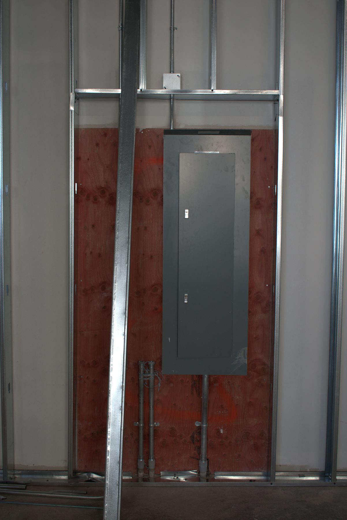 Electrical panel mounted on plywood backing within unfinished metal stud wall — Leela Spa (West District)