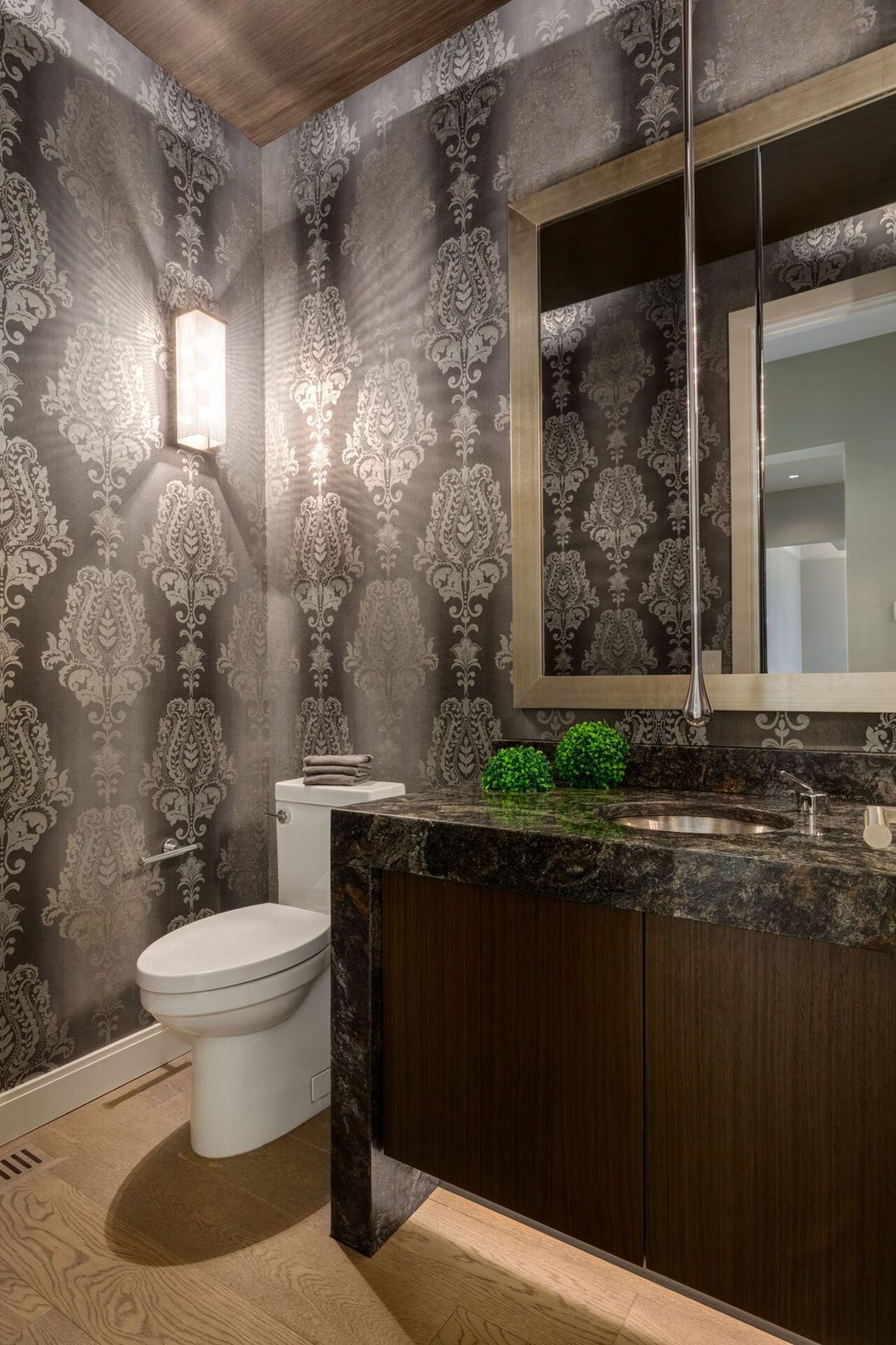 Elegant powder room with damask wallpaper, dark vanity, and toilet — The Cellar