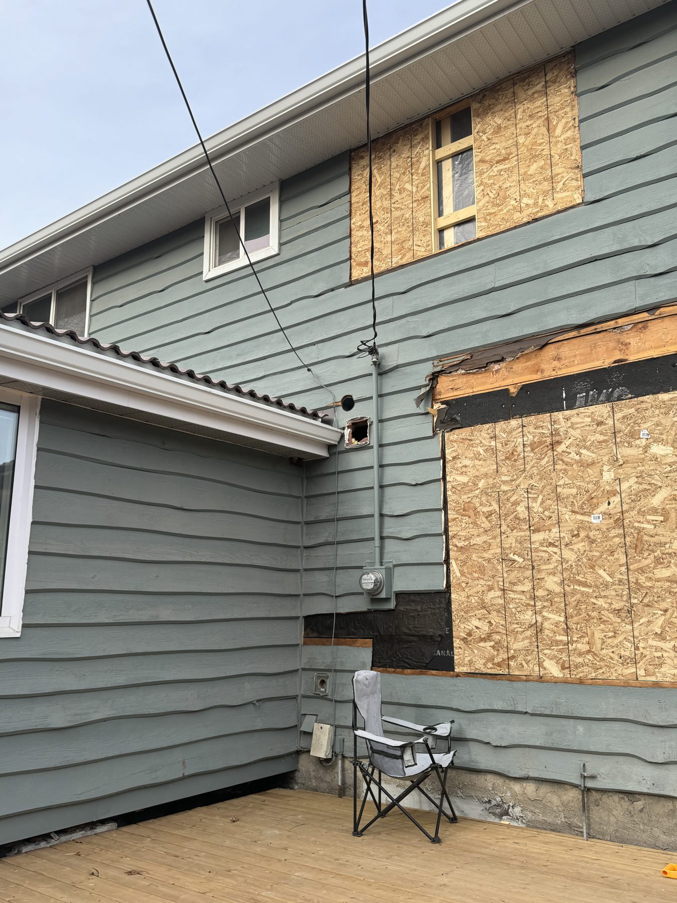 House siding under repair, windows boarded with OSB — 188 Lake Adams Crescent SE, Calgary