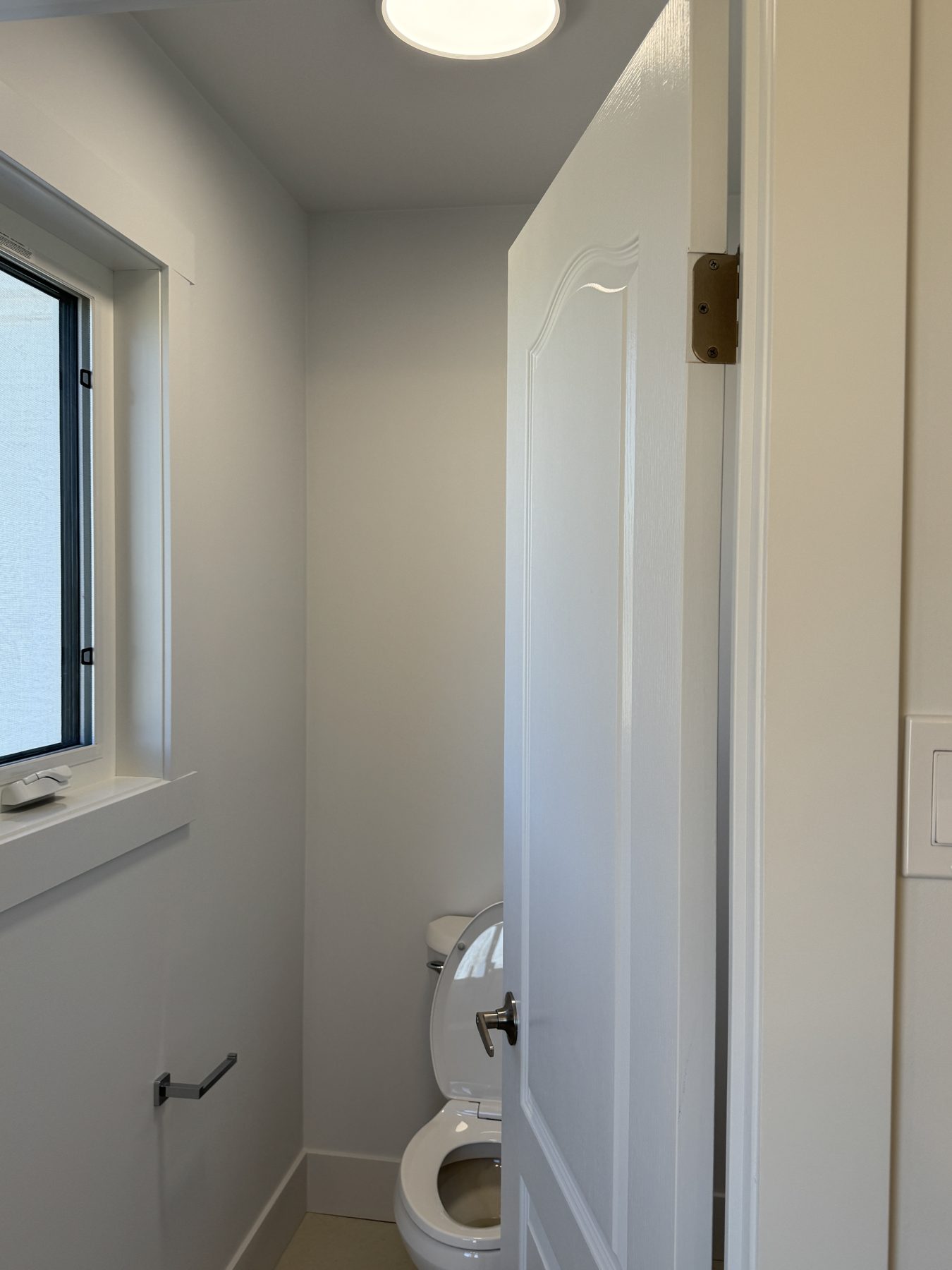 Half-bath renovation with white toilet, door ajar, and window — 14 Lochend Drive, Cochrane
