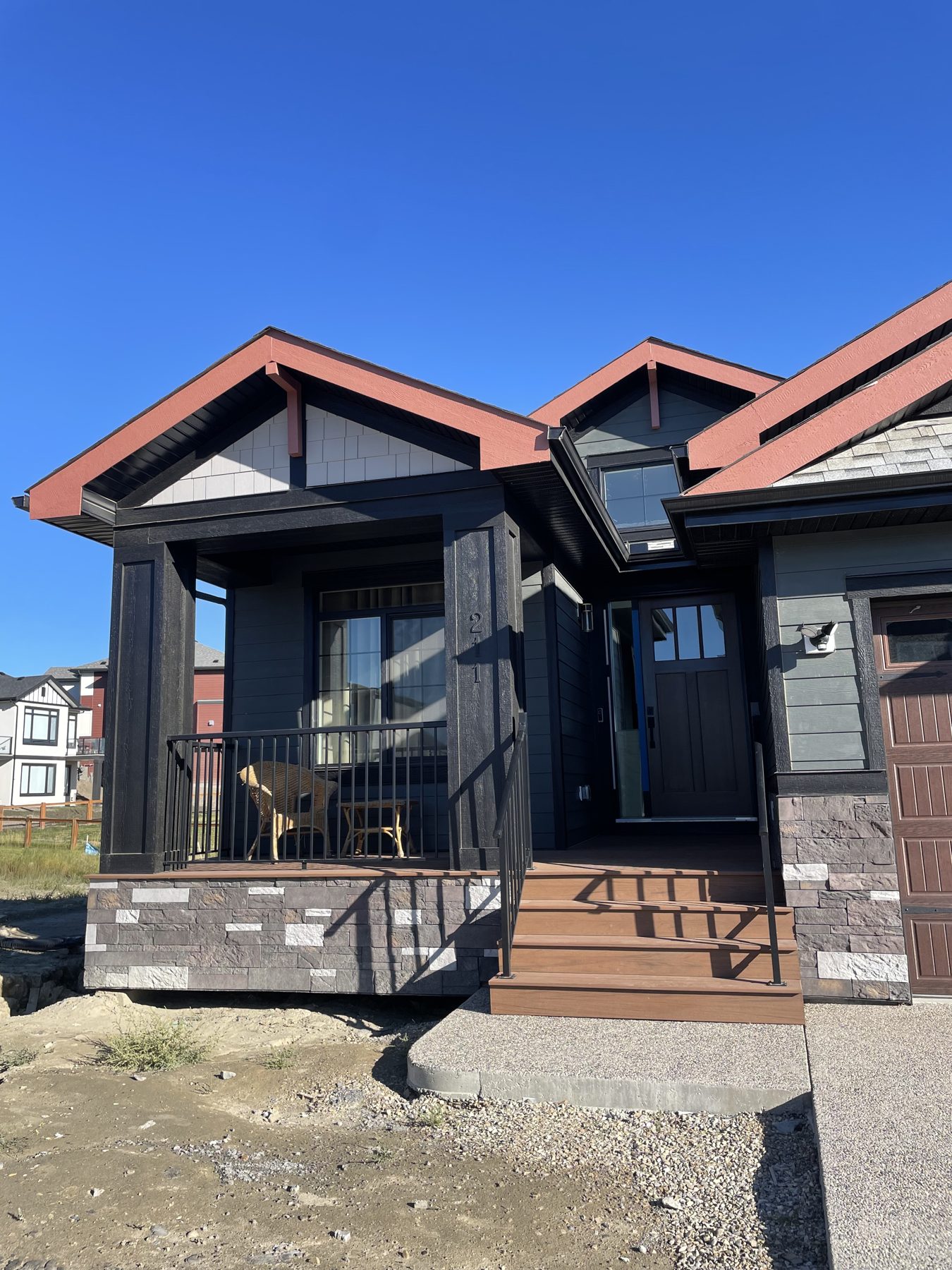 New house exterior with stone facade, dark siding, and wood deck stairs — 211 Blackstone Rd