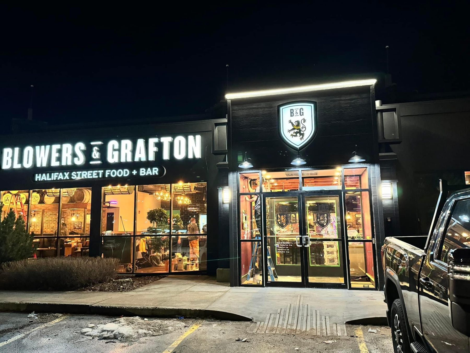 Restaurant exterior night scene with entrance, signage, and workers on ladders — Blowers and Grafton (Shawnessy)