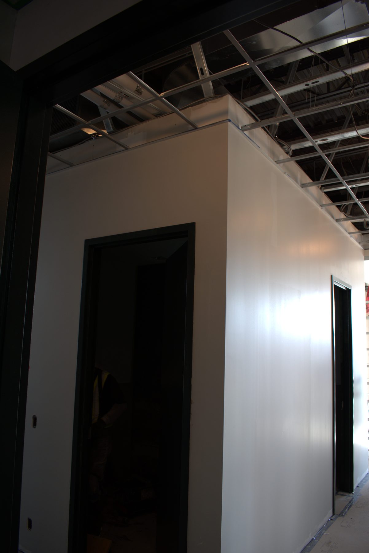 Interior walls painted white, exposed ceiling grid, dark doorways at construction site — ONE8T (West District)