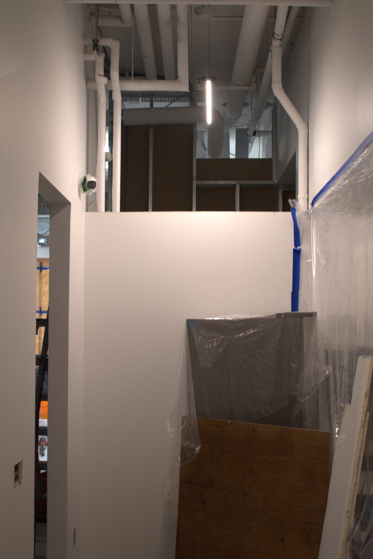 Interior construction phase, pipes, drywall, protective sheeting, and construction materials visible — Big Buns (Bowness)