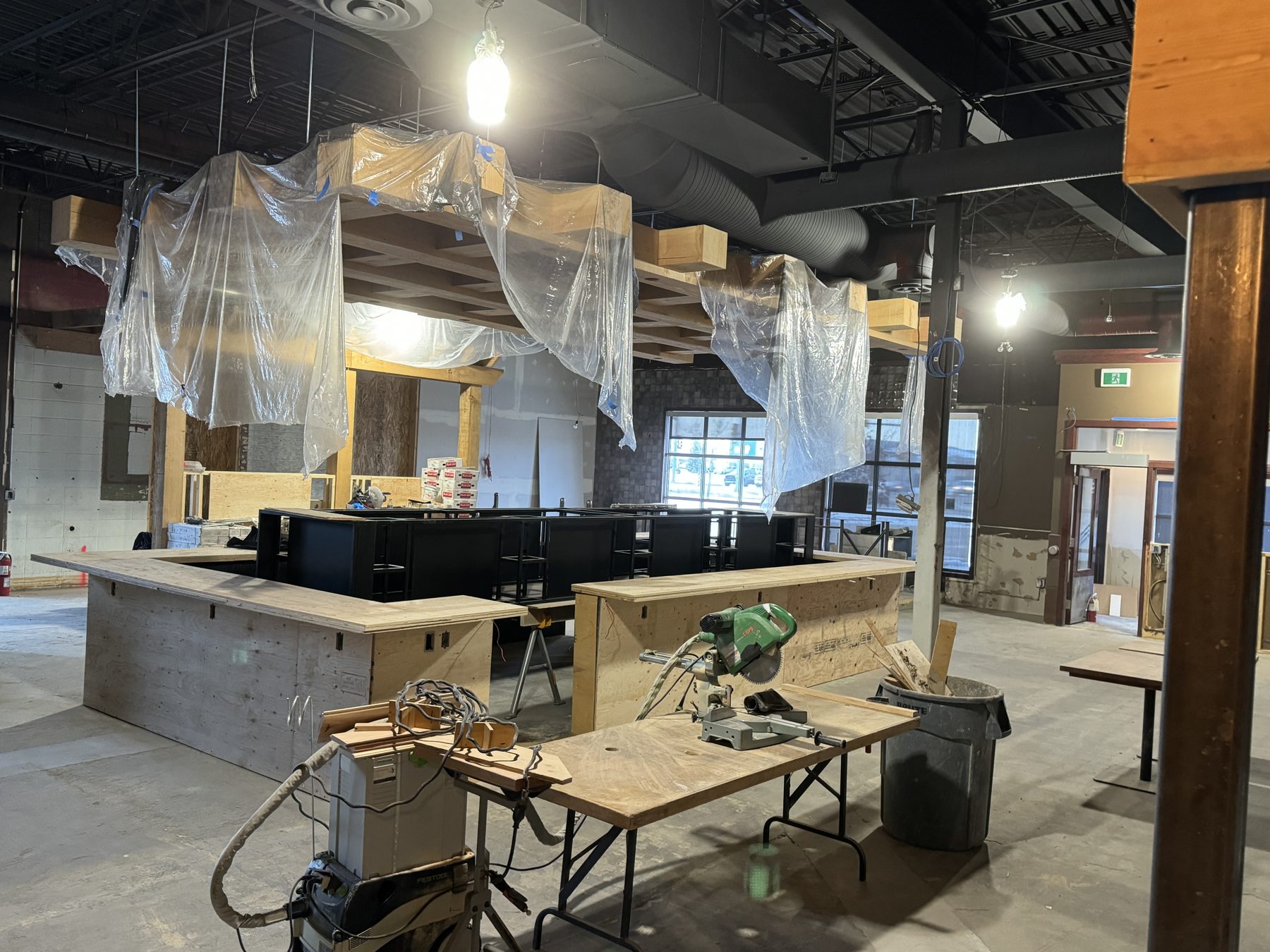 Construction site with plywood bar, chop saw, and plastic-covered ceiling beams — Blowers and Grafton (Medicine Hat)