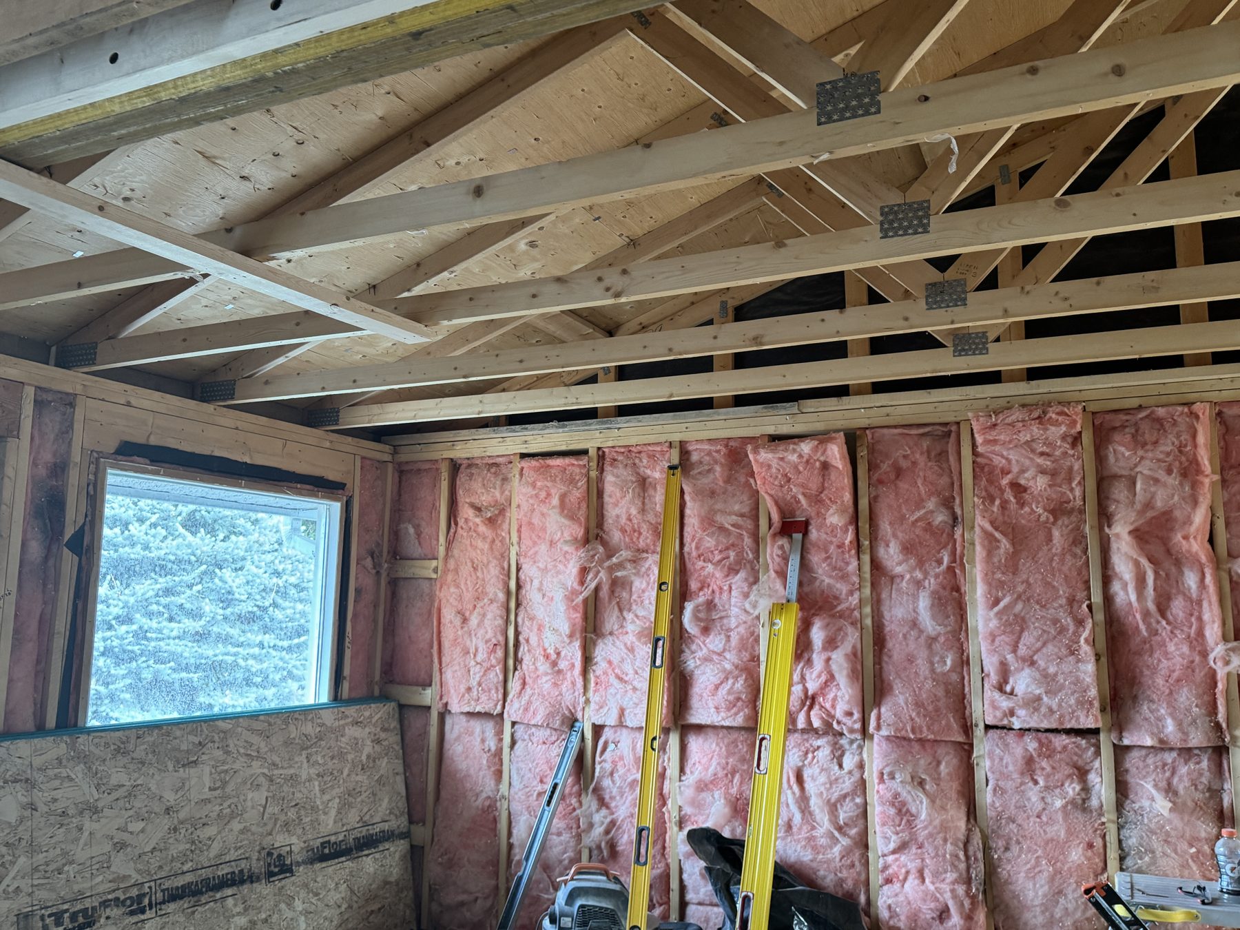 Room under construction with pink insulation and exposed wooden ceiling joists — 188 Lake Adams Crescent SE, Calgary