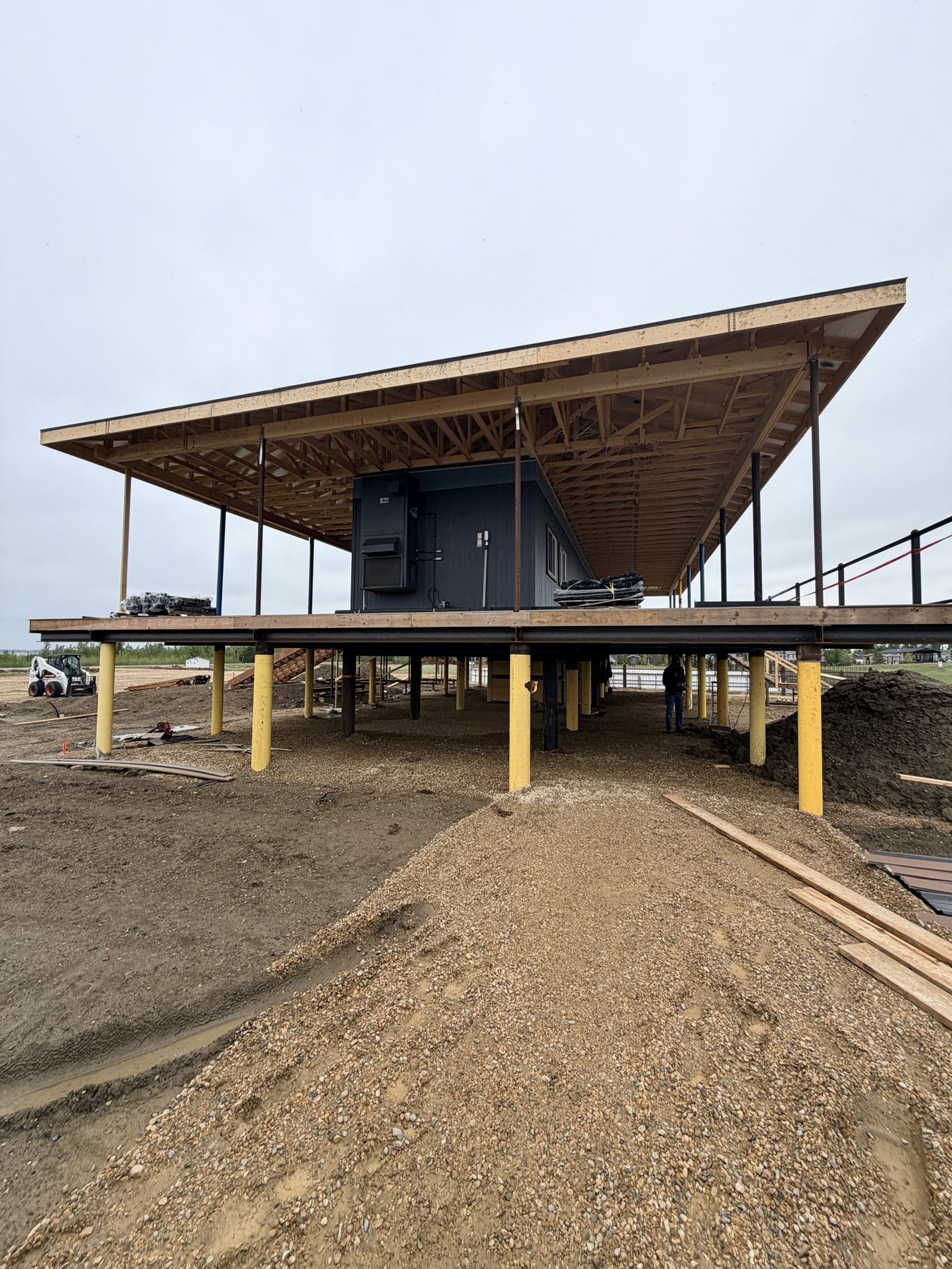 Elevated building under construction with exposed wood trusses and gray exterior — Sandy Point (Club House)