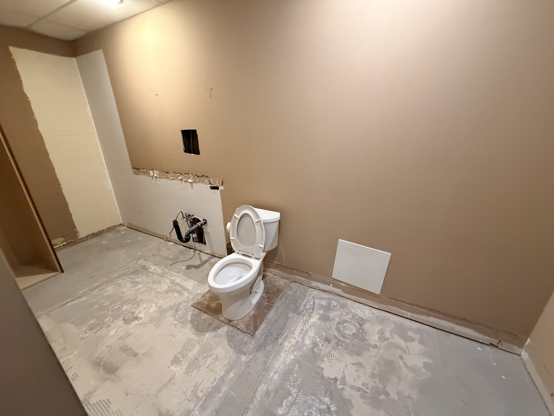 Renovating bathroom with toilet, exposed pipes, and unfinished floor — The Barron Venue