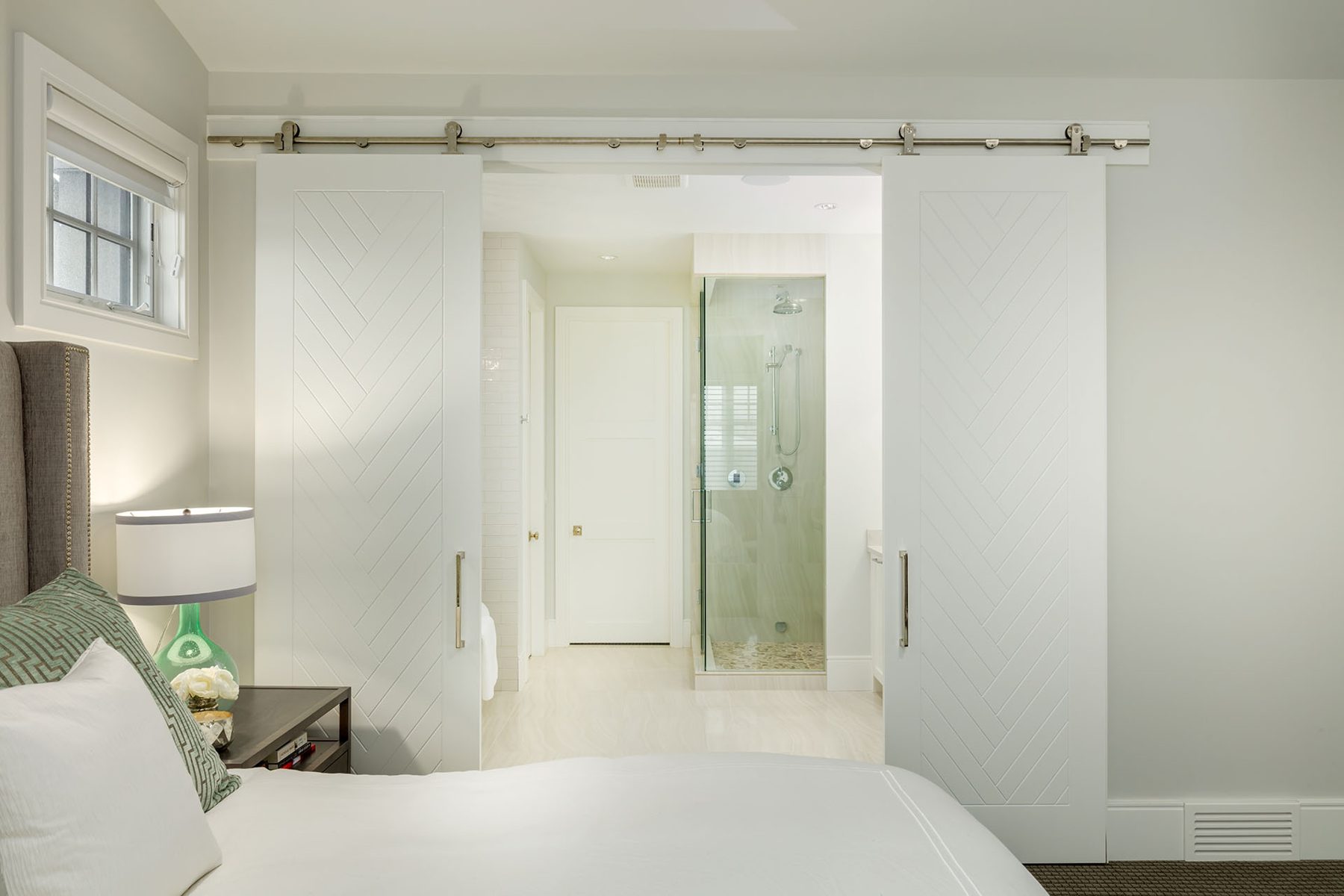 Bedroom, white barn doors open to tiled bathroom with glass shower — Cleret Velour
