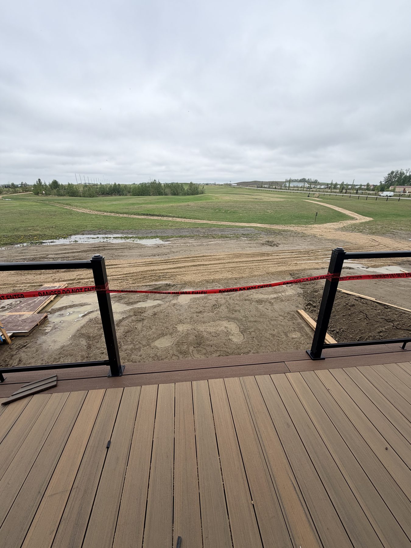 New deck framing with caution tape, mud, and undeveloped lot — Sandy Point (Club House)