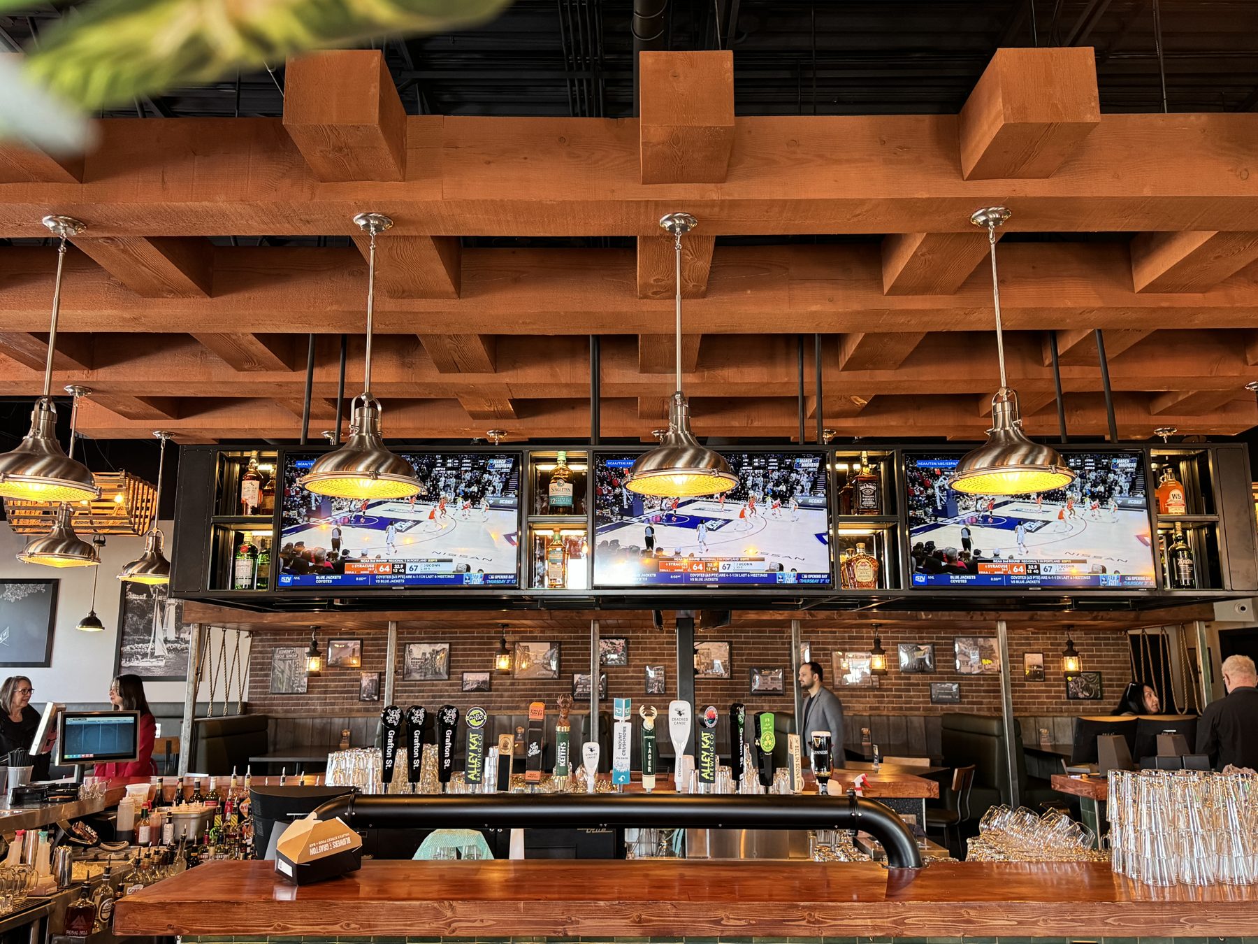 Bar with TVs showing basketball, beer taps, wood beams, and pendant lights — Blowers and Grafton (Medicine Hat)