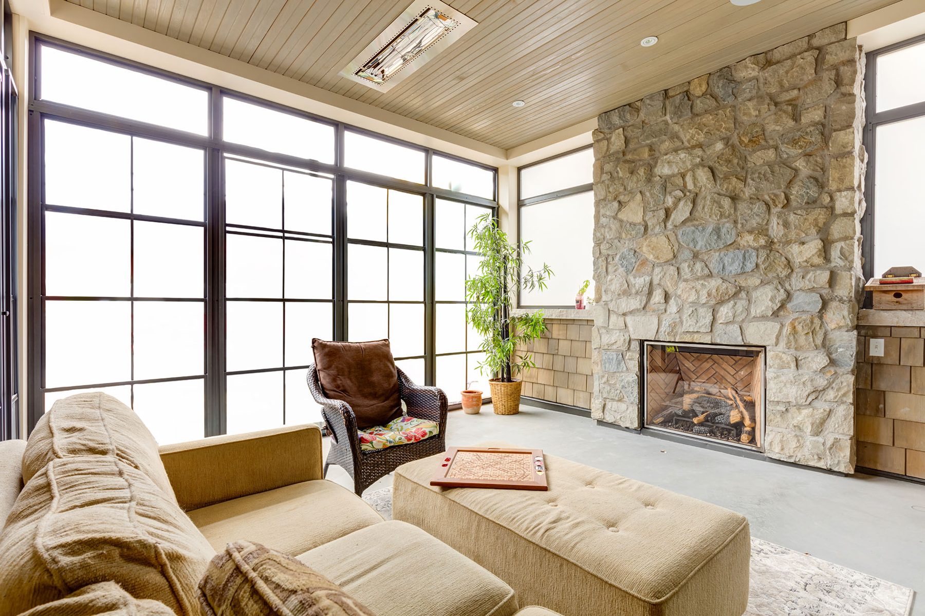 Sunroom with stone fireplace, large windows, and comfortable seating — Artista