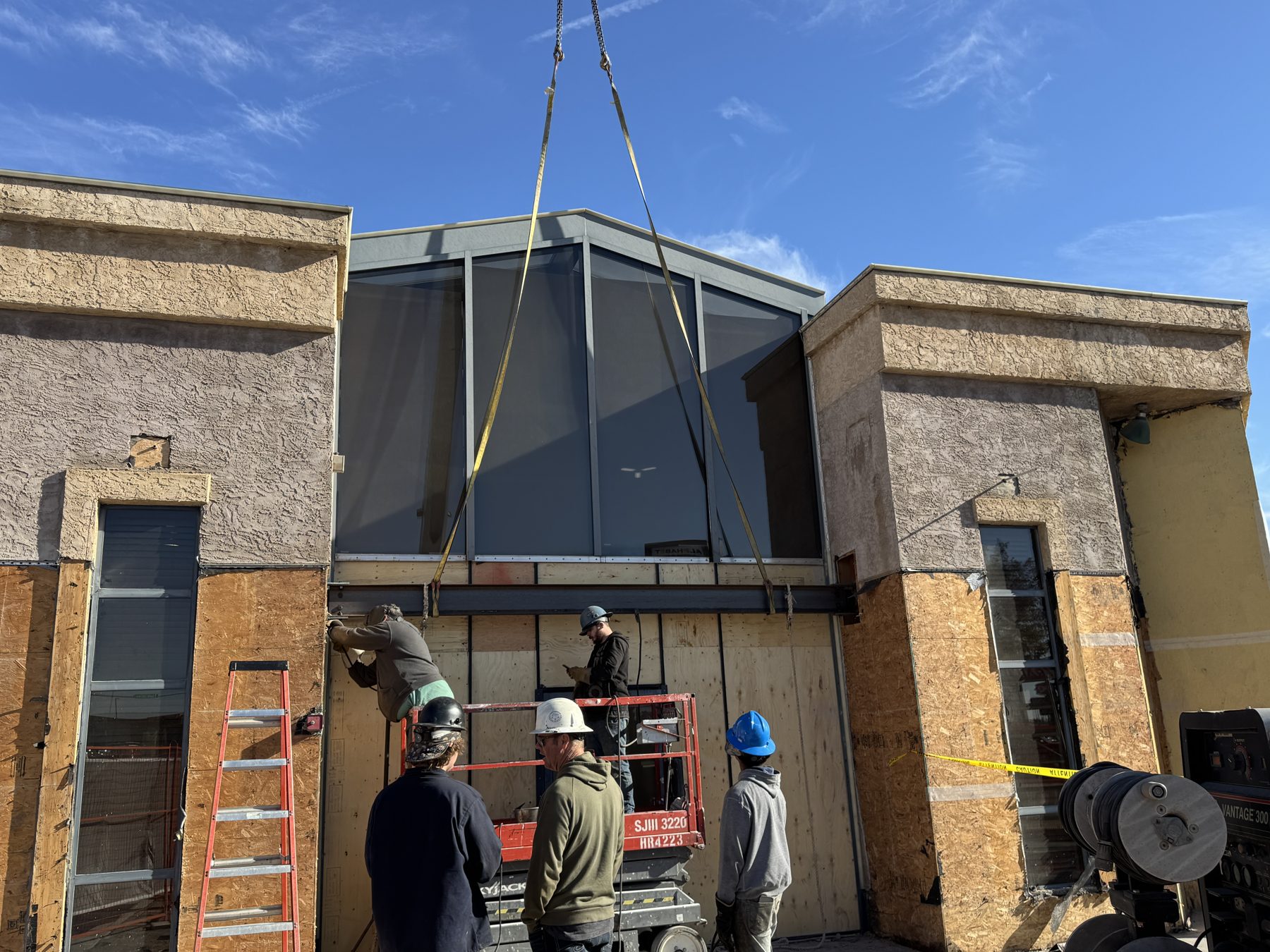 Crane lifting steel beam at construction site with workers below — Blowers and Grafton (Red Deer)