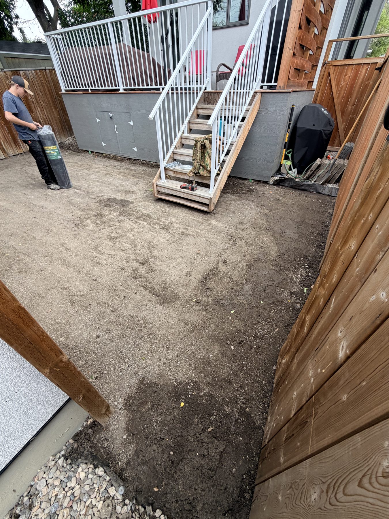 Worker unrolls landscape fabric next to wooden deck stairs — 3505 41 Street SW, Calgary