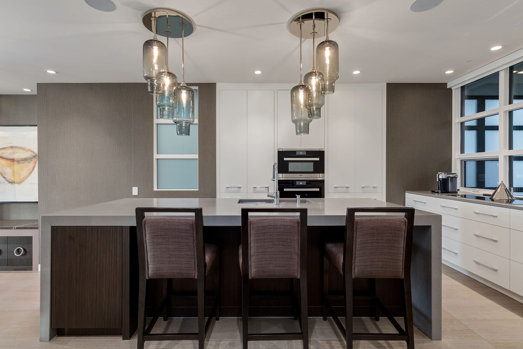 Modern kitchen island with bar stools, pendant lights, and built-in appliances — Skyline