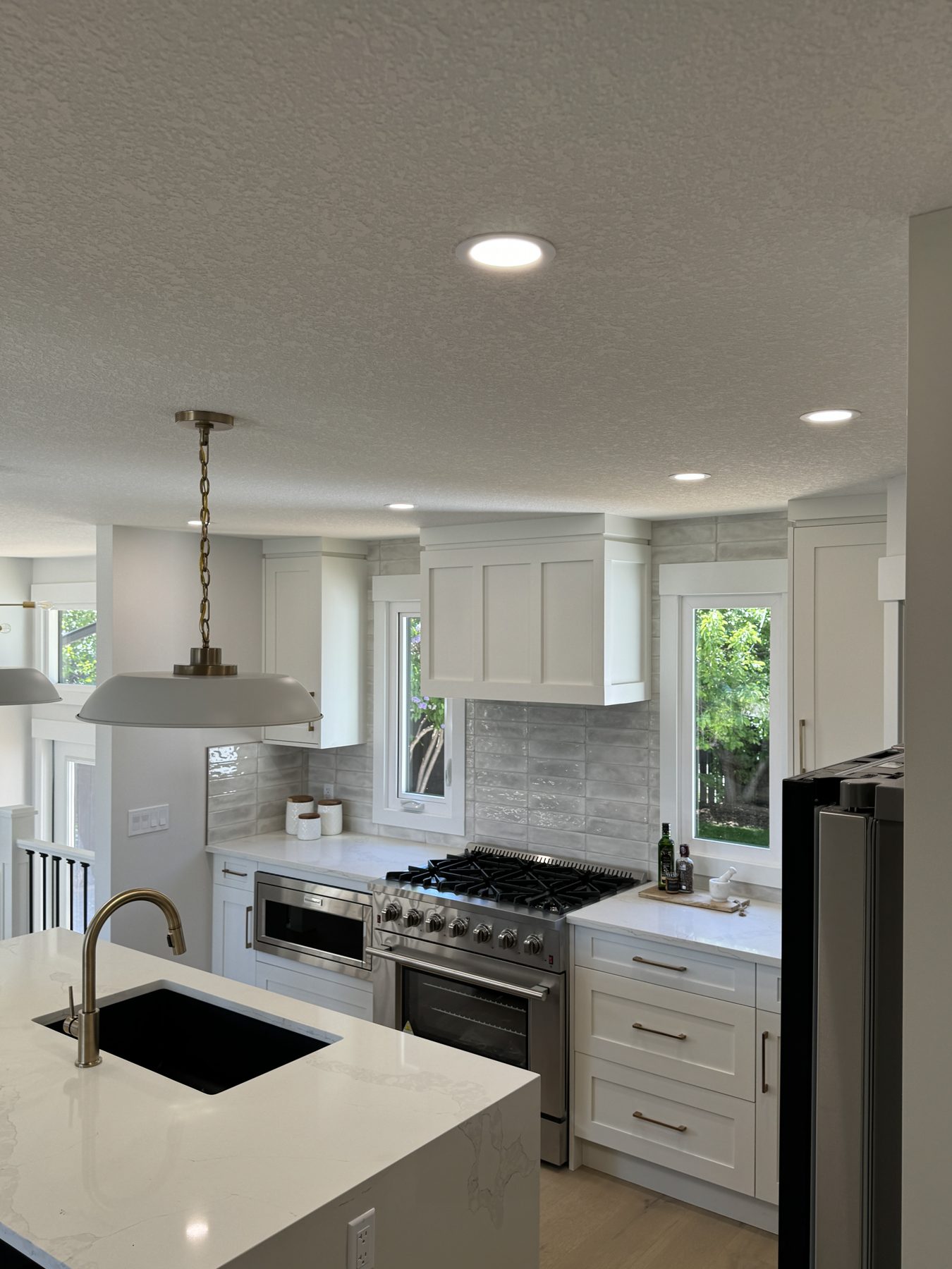Kitchen island with sink, stainless steel range, white cabinets, gray tile backsplash — Lake Bonavista