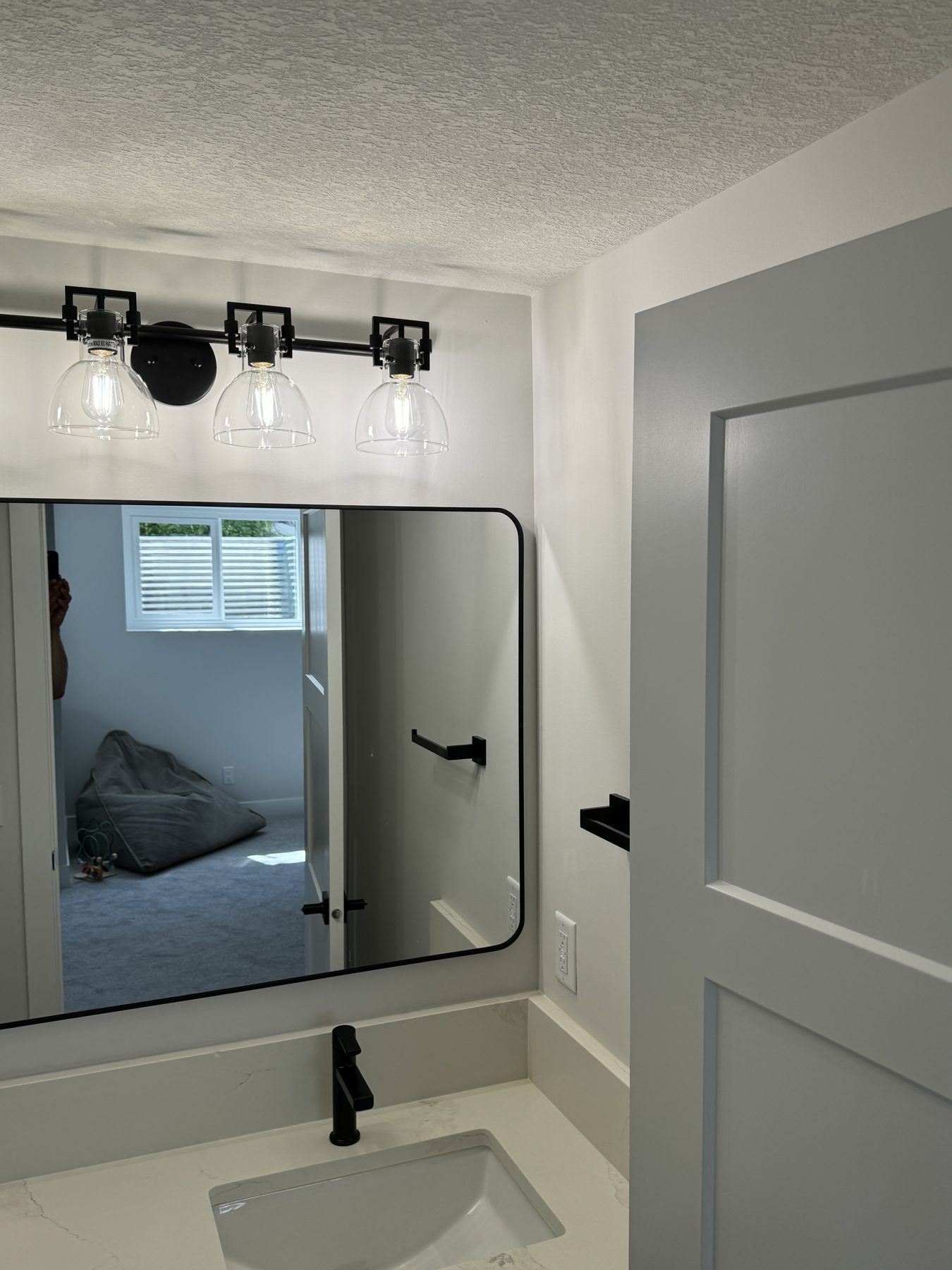 Modern bathroom vanity with black fixtures and clear glass light sconces — Lake Bonavista