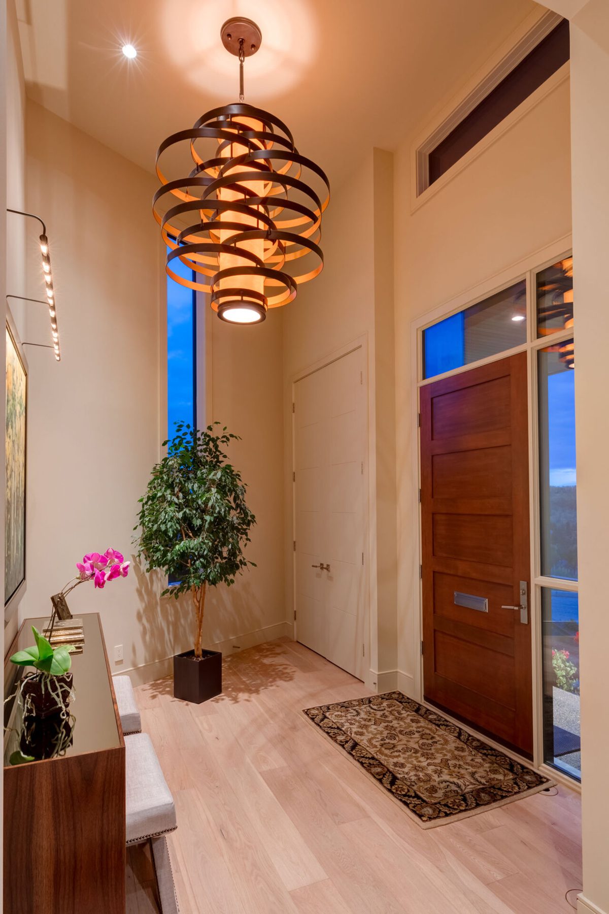 Entrance hall with wood door, light wood floors, and large statement light fixture — Evolution