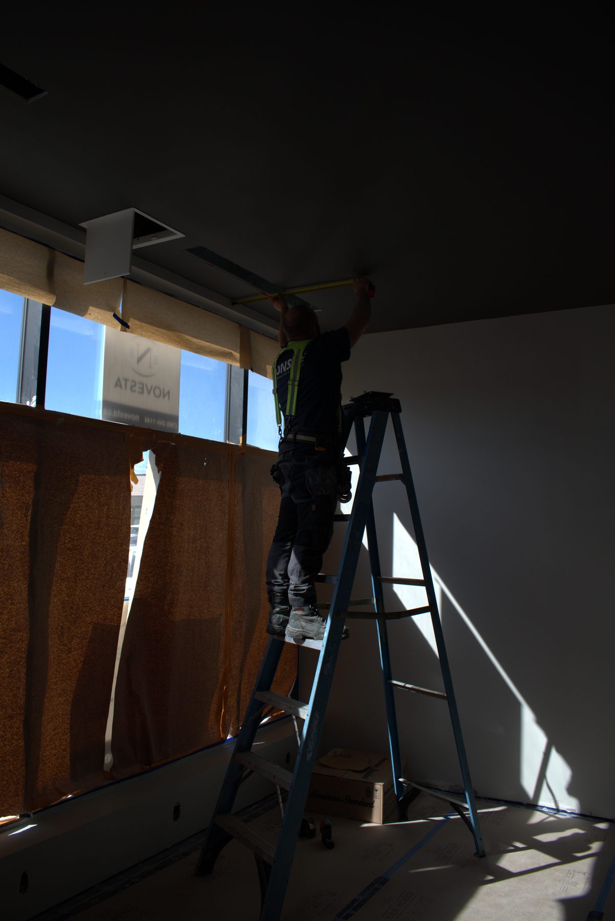 Worker on ladder measures ceiling for new light fixture installation — ONE8T (West District)