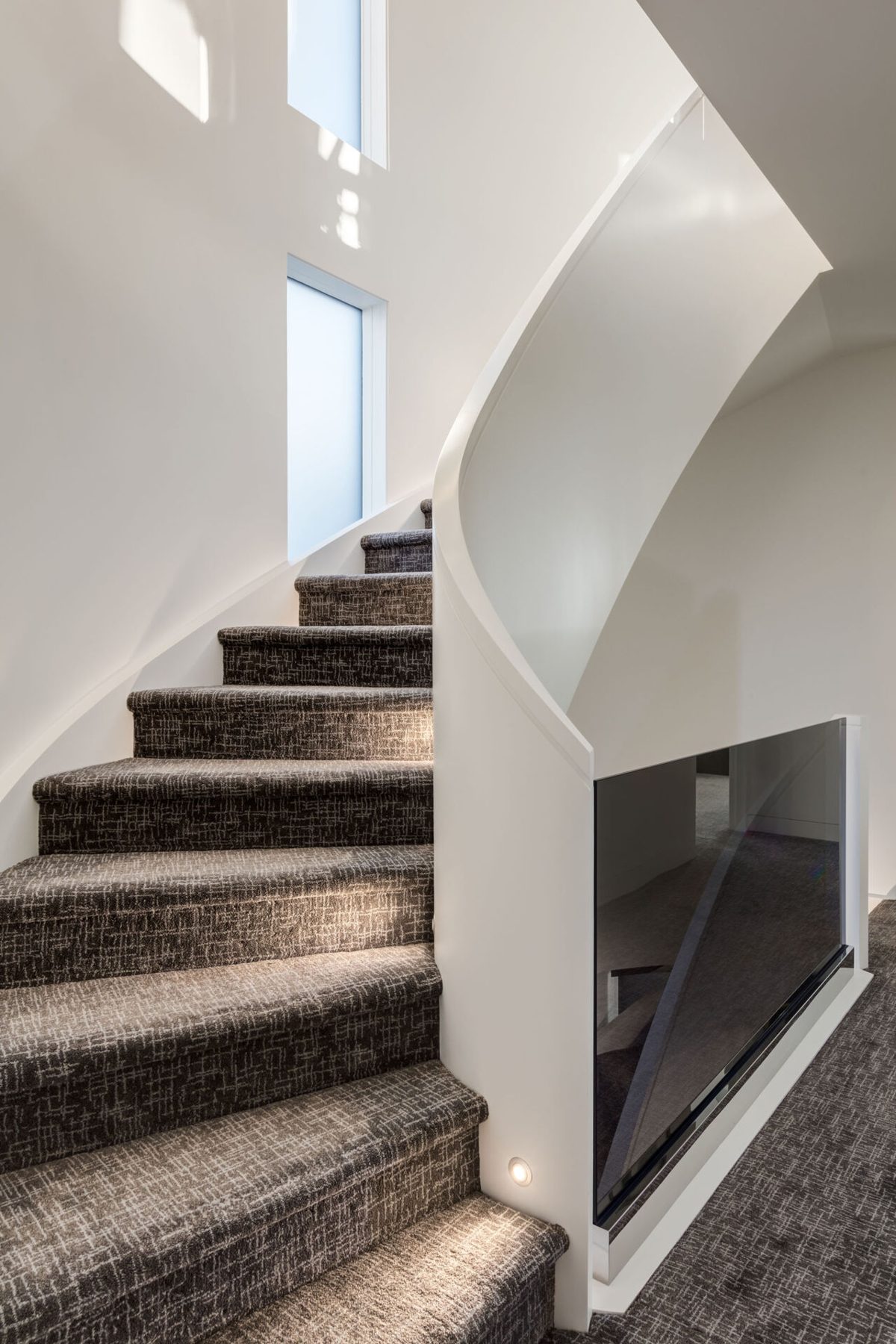 Modern curved staircase with carpeted steps and glass railing — Skyline