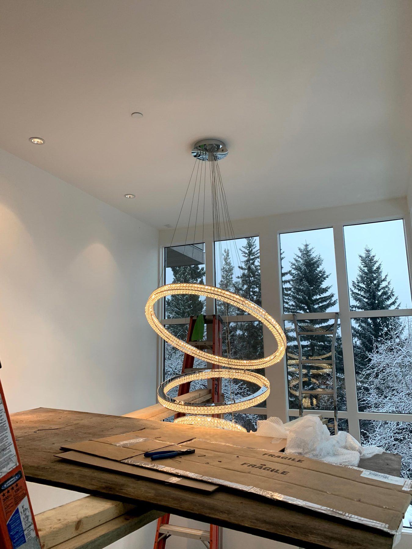 Modern crystal chandelier installation in room with large windows and snow — Pump Hill