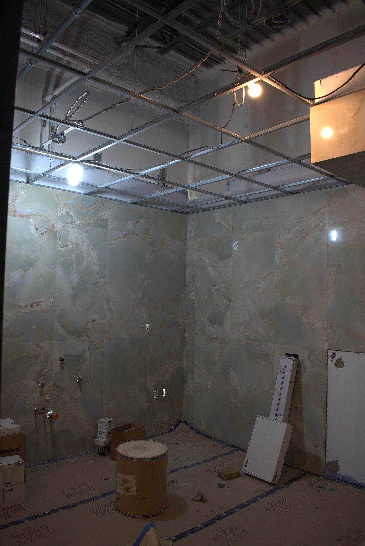 Green marble tiled shower stall under construction with exposed ceiling grid — ONE8T (West District)