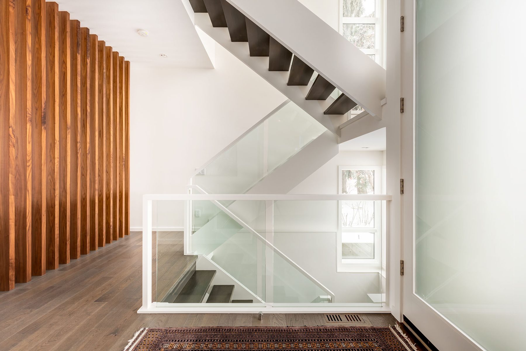 Modern staircase with glass railings and wood accent wall — Casa Blanca