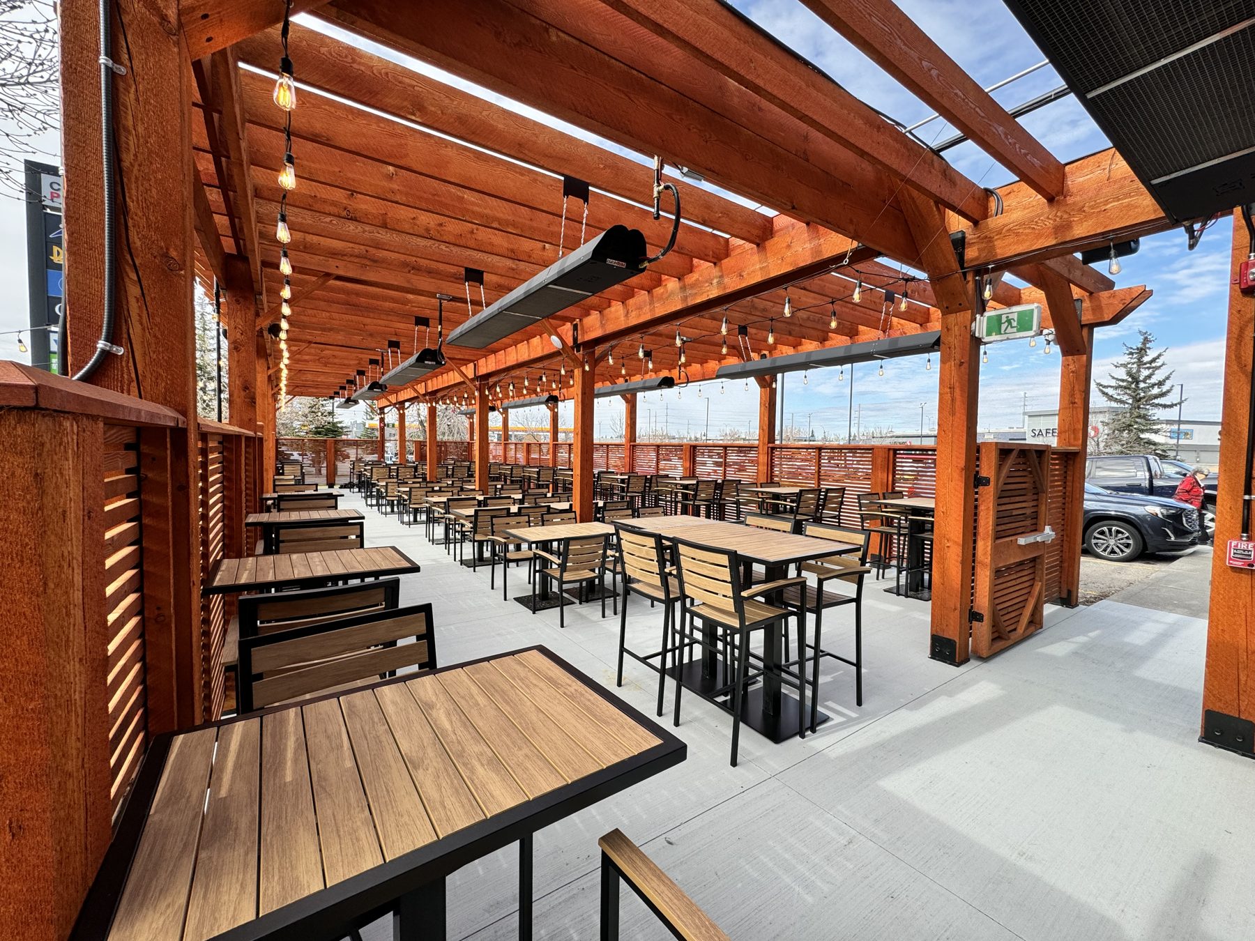 Wooden pergola patio with tables, chairs, string lights, and heaters — Blowers and Grafton (Medicine Hat)