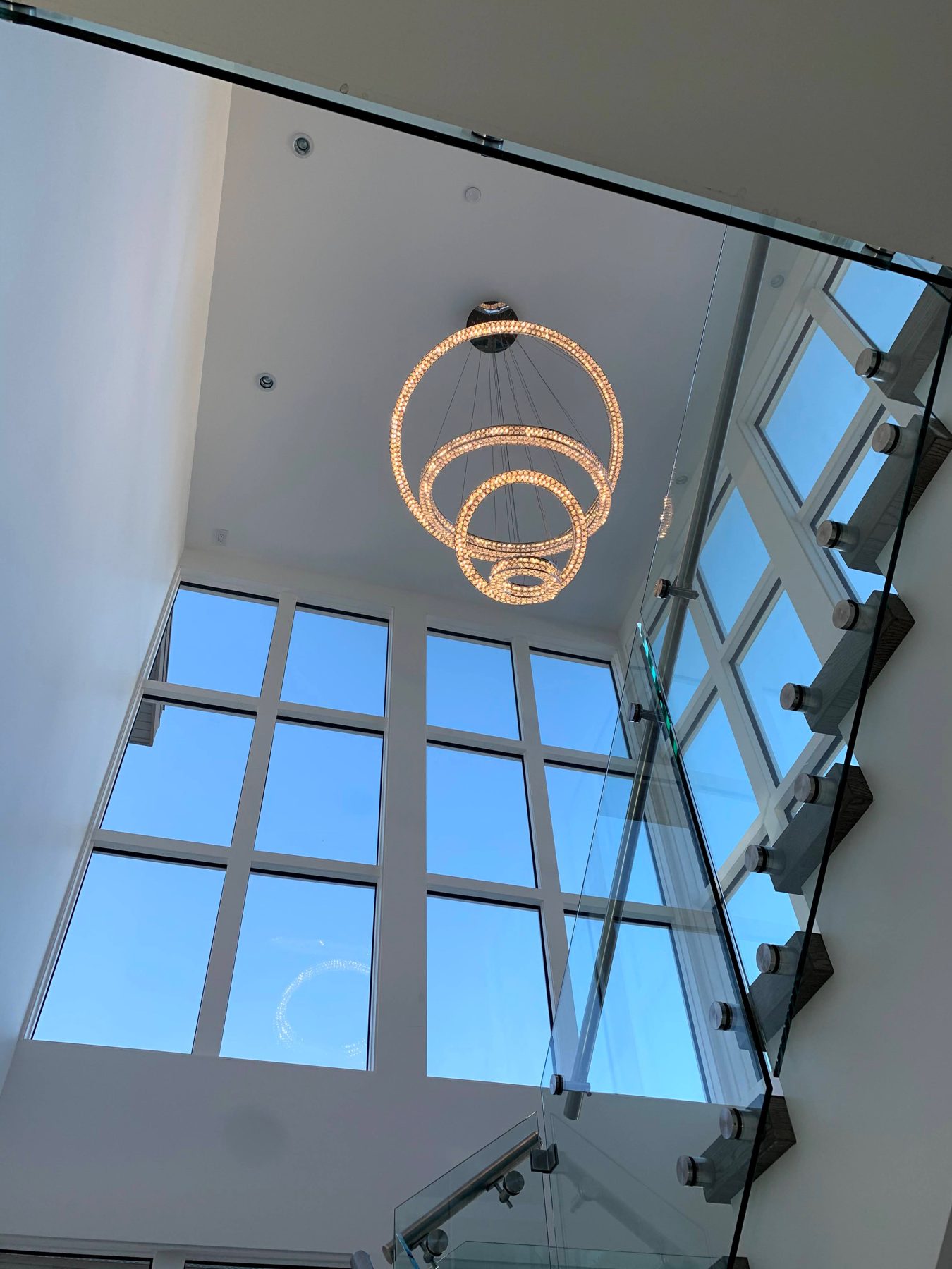 Modern entryway with crystal chandelier and glass staircase railing — Pump Hill