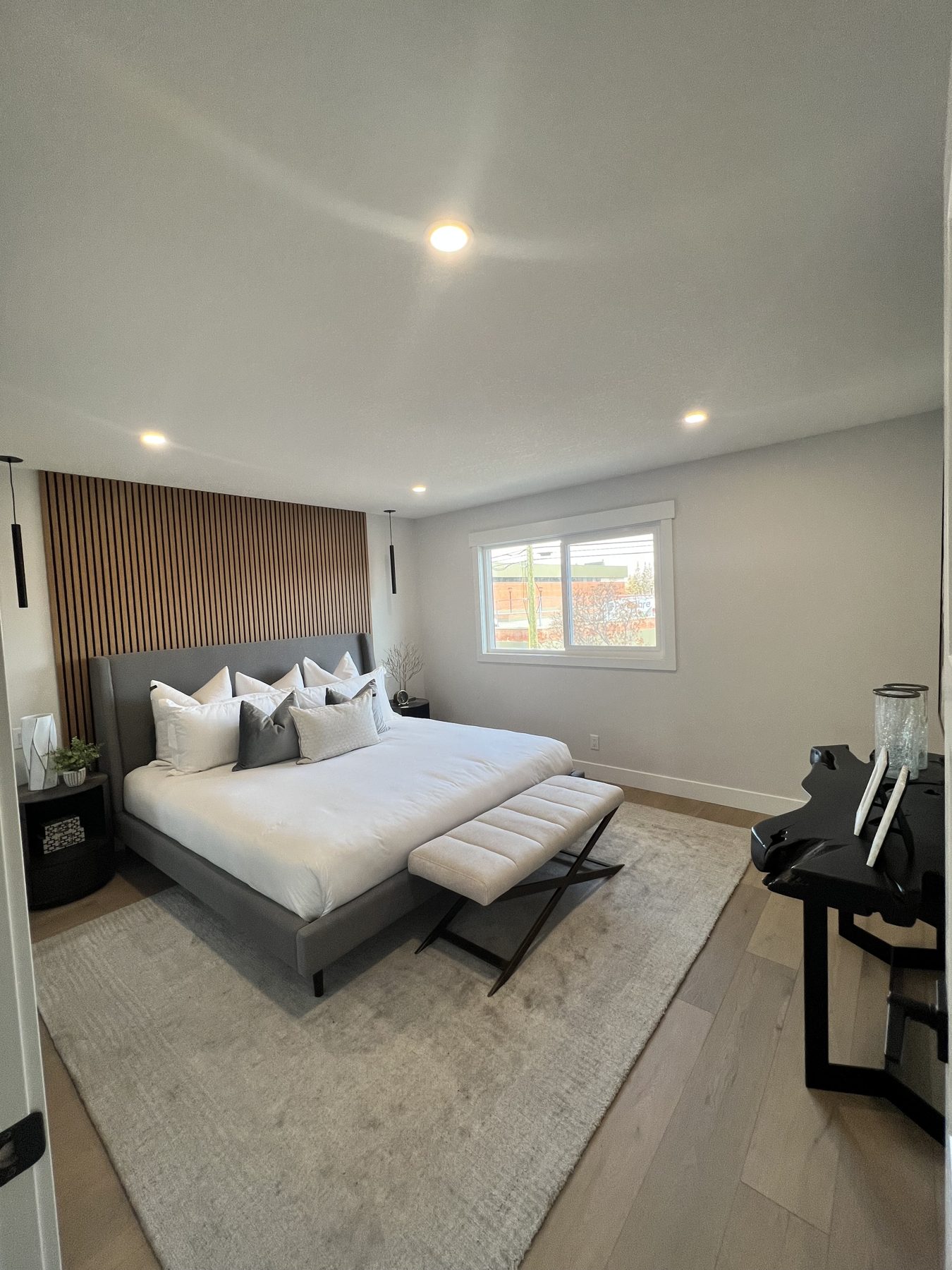 Modern bedroom with wood slat wall, king bed, and minimalist decor — 720 Lake Twintree Crescent SE, Calgary