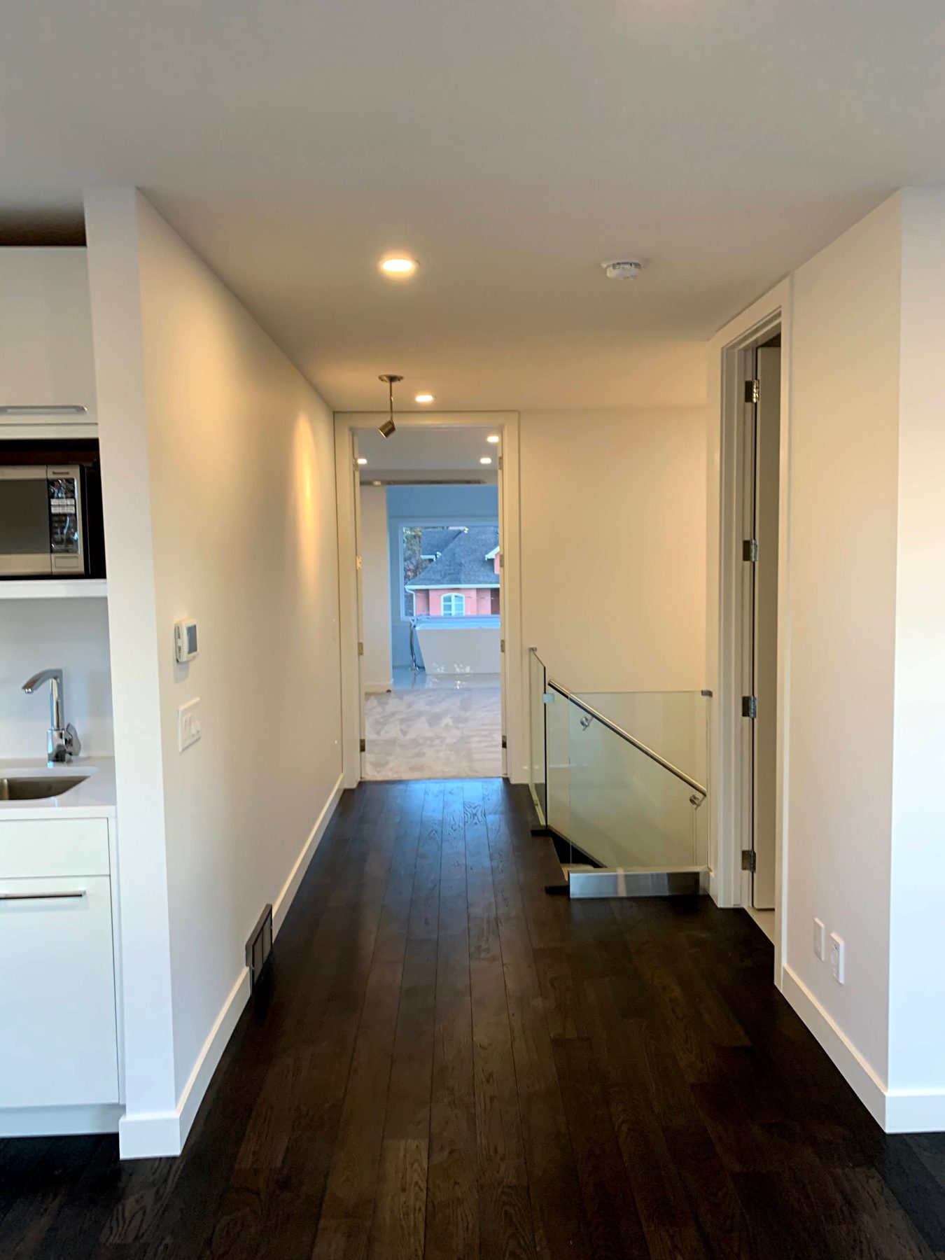 Modern hallway with dark wood floors and glass staircase railing — Lake Bonavista