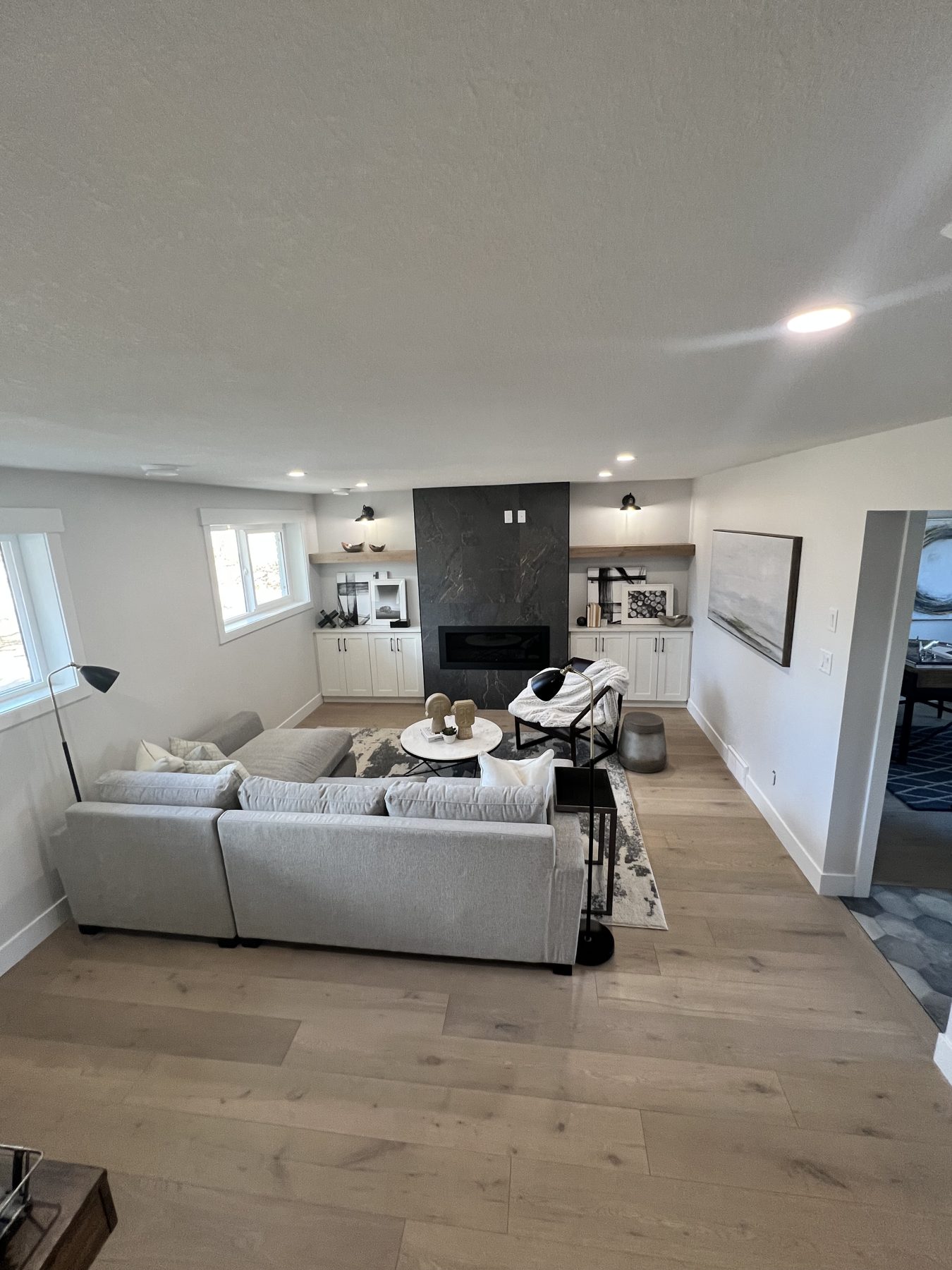 Living room with fireplace, light wood floors, and sectional sofa — 720 Lake Twintree Crescent SE, Calgary