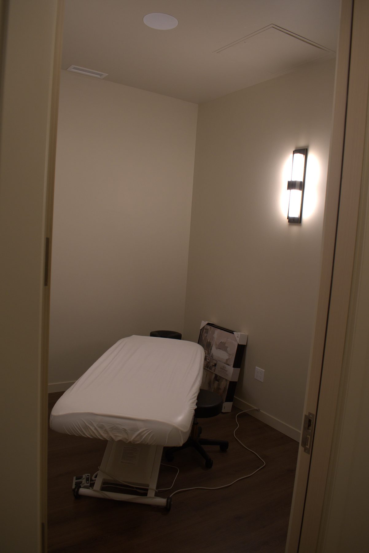 Massage room with white covered table, artwork, and wall sconce — Leela Spa (Bankers Hall)