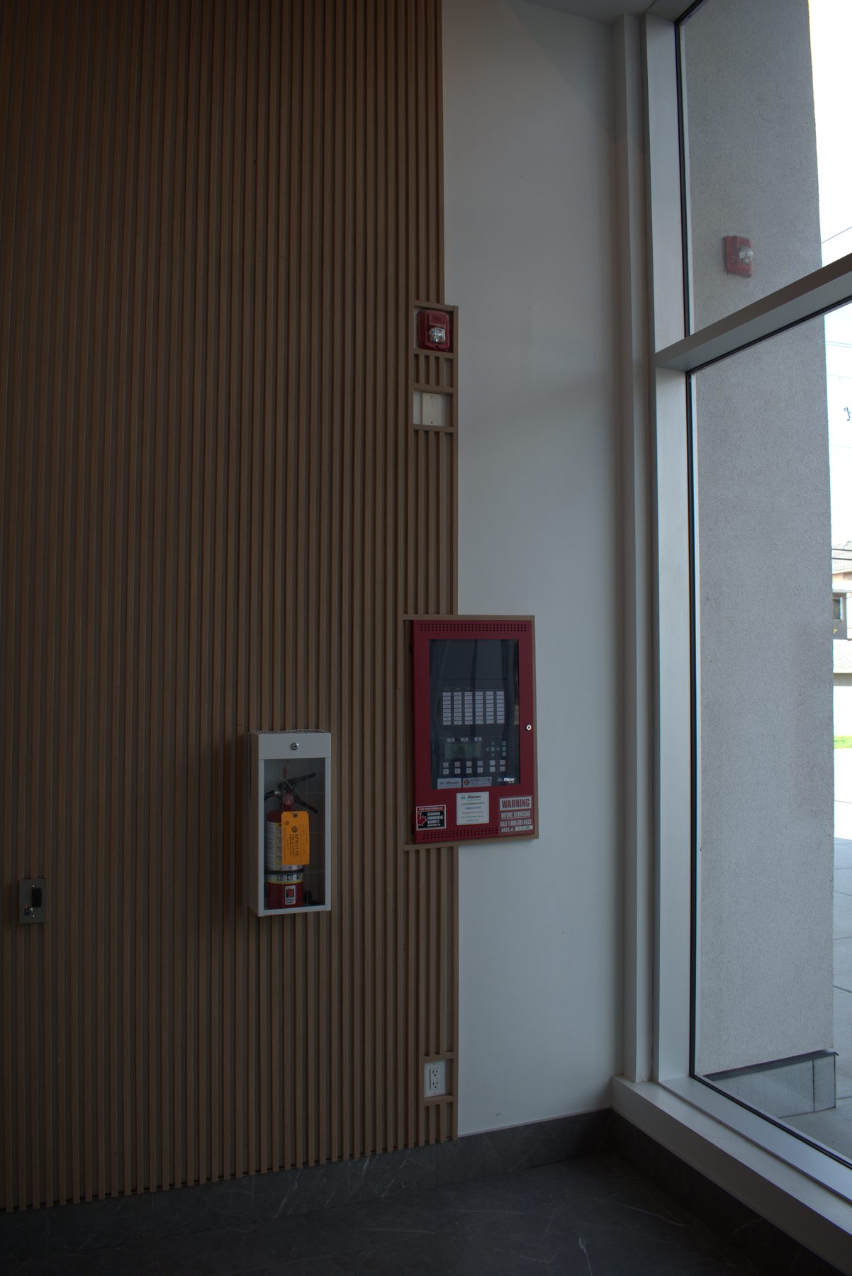 Fire alarm panel, extinguisher, and wood slat wall in lobby — Big Buns (Bowness)