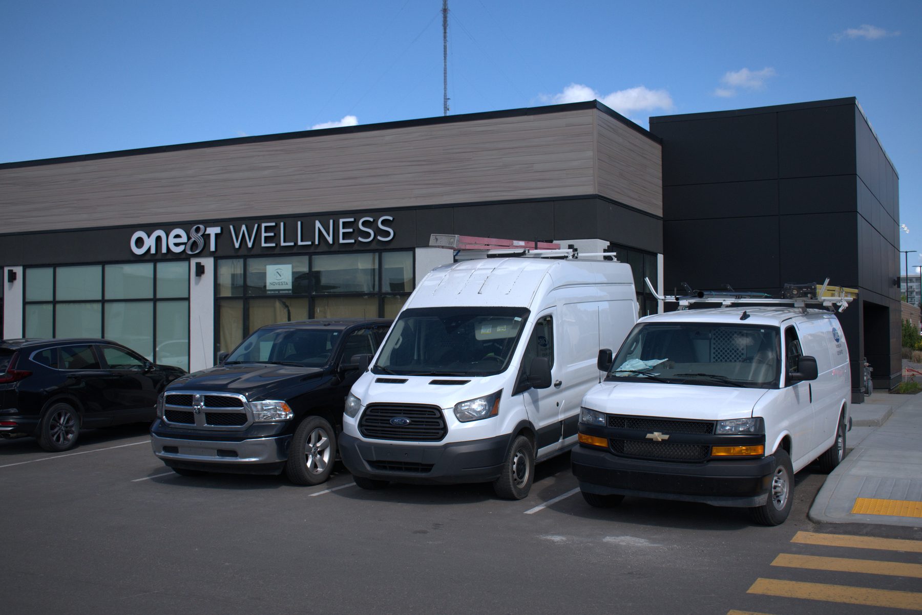 Construction vans parked outside a building with "OneST WELLNESS" signage — ONE8T (West District)
