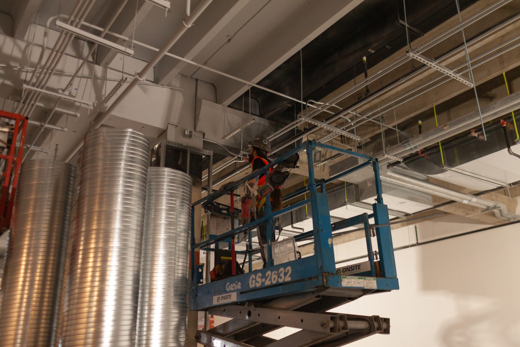 Construction worker on lift installs pipes near large metal ducts — Old Navy Chinook by Onsite Contracting Services