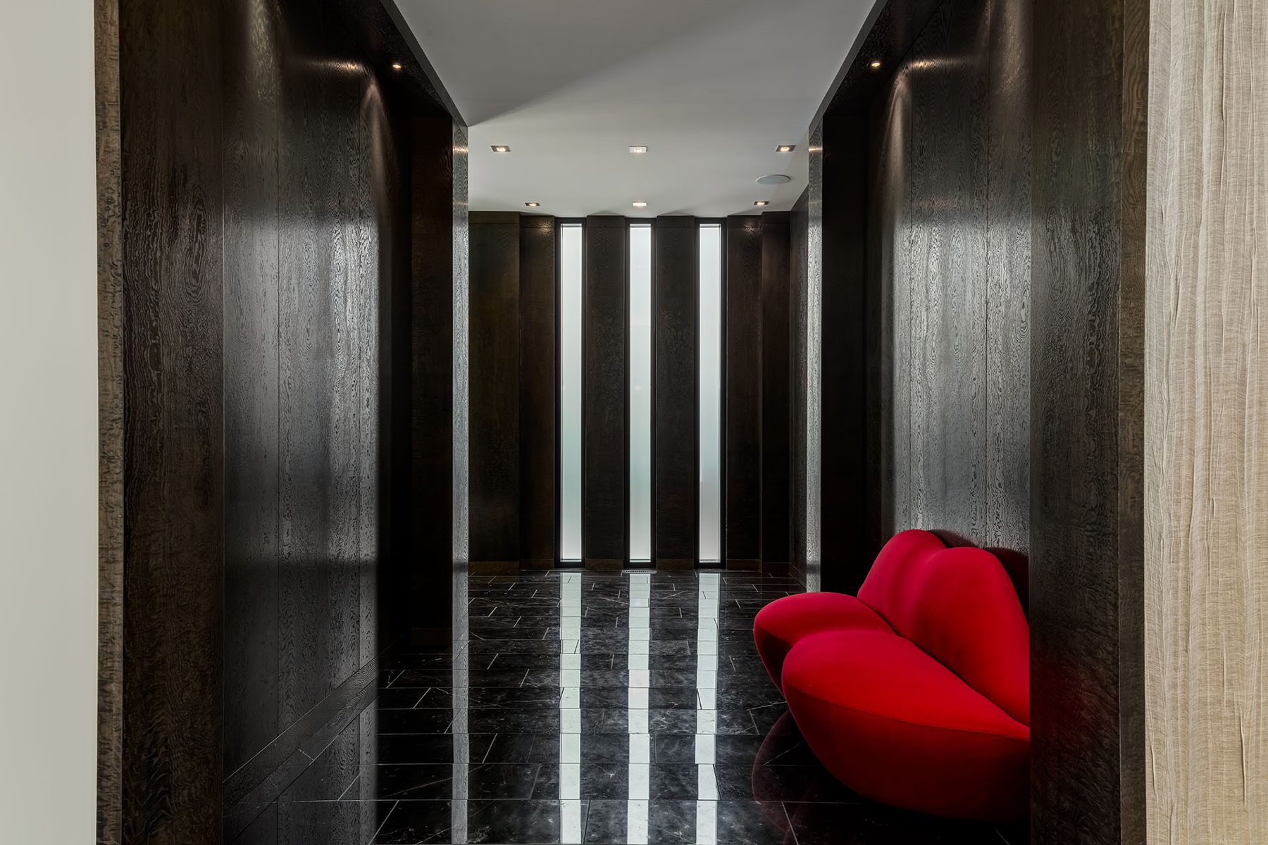 Hallway with dark wood panels, polished floor, and red lip sofa — Modern Family