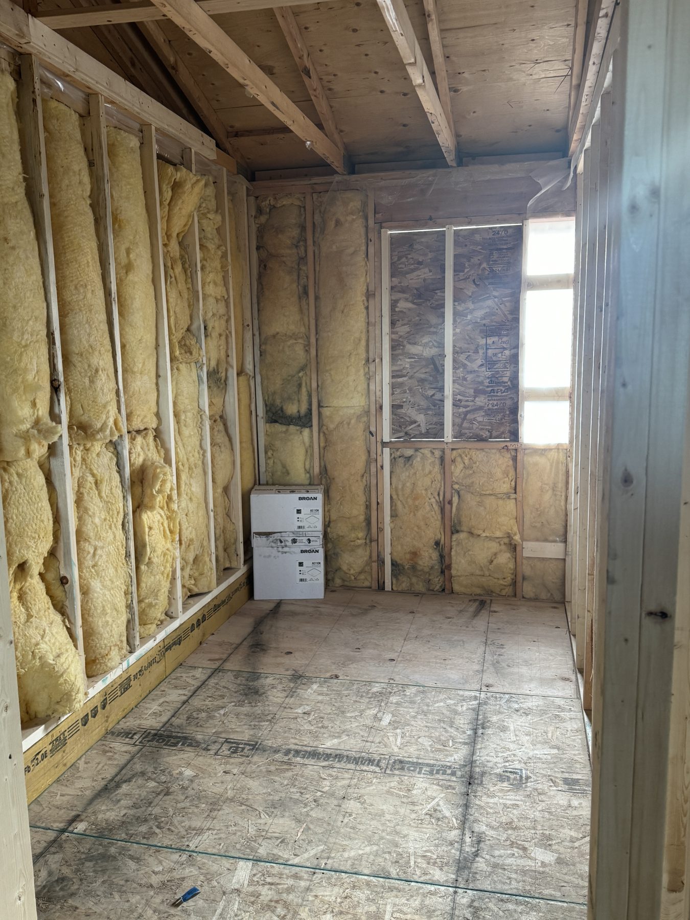 Interior room framing with fiberglass insulation, plywood flooring, and two boxes — 188 Lake Adams Crescent SE, Calgary