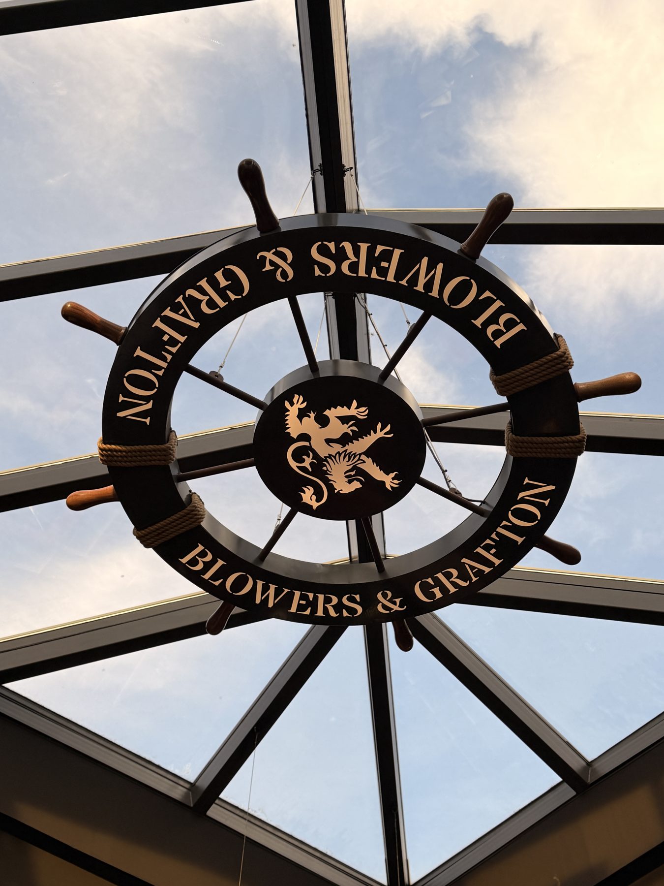 Ship's wheel sign hanging from skylight, lettering and dragon emblem — Blowers and Grafton (Red Deer)