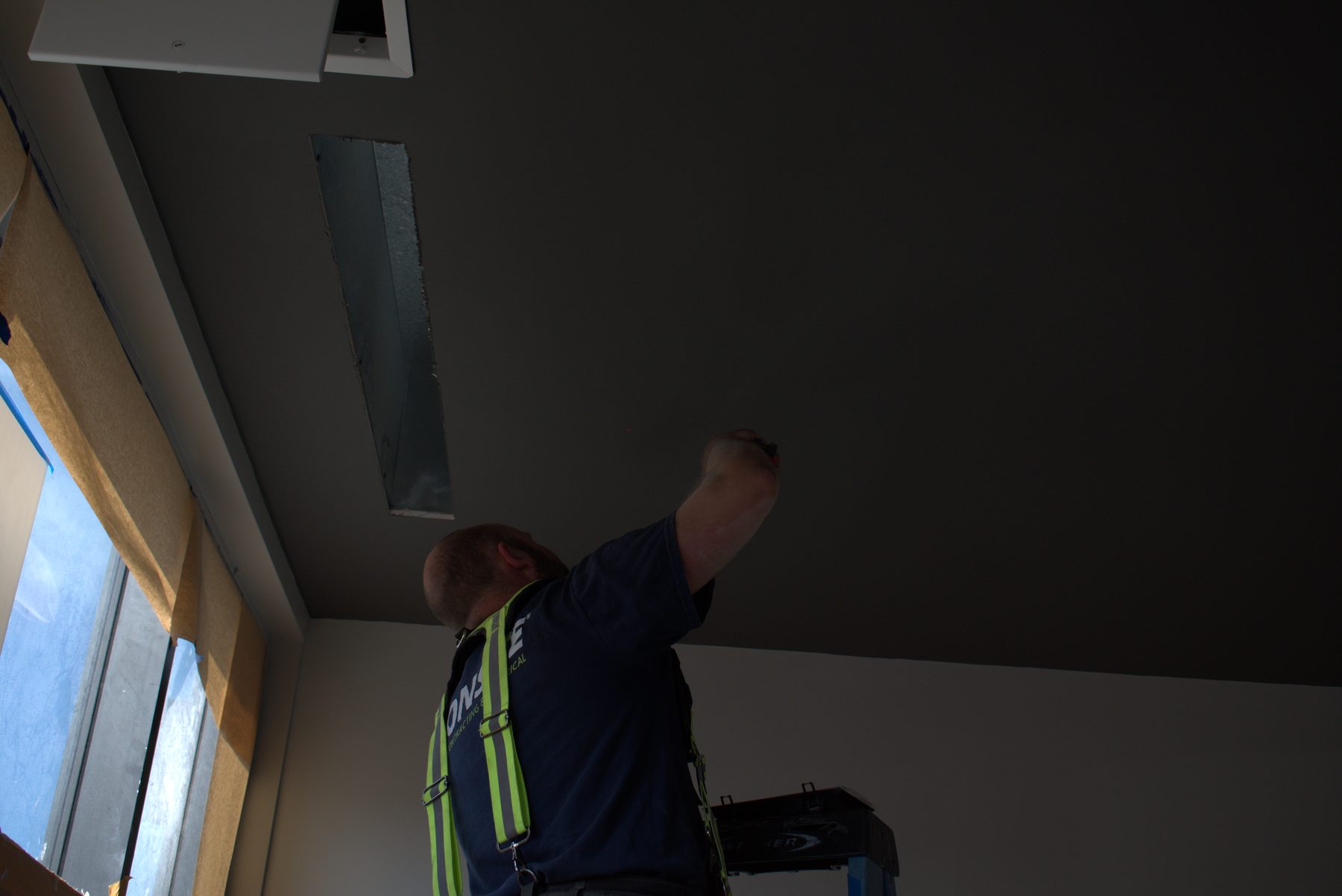 Worker on ladder installs ceiling vent, plastering underway — ONE8T (West District)