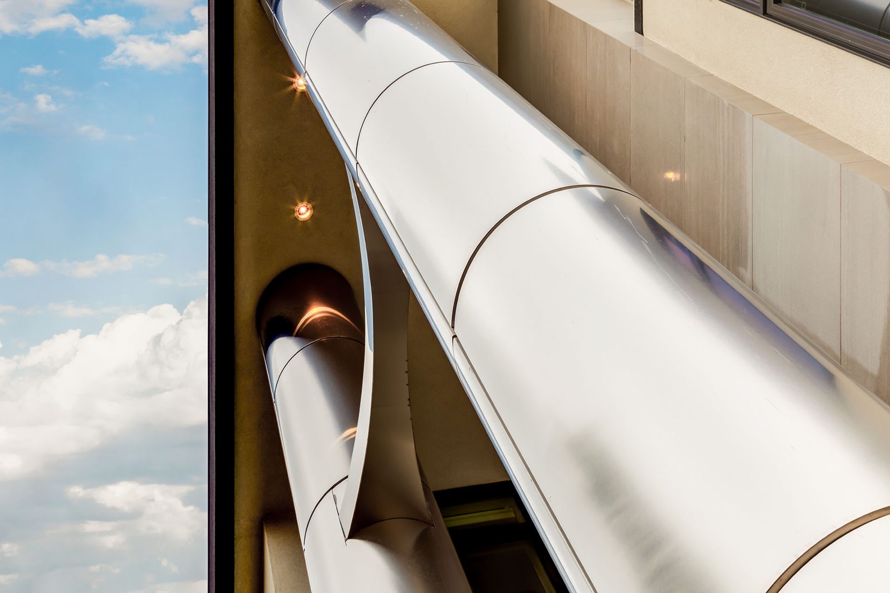 Modern exterior with large, polished silver pipes and recessed lighting — Timeless Form