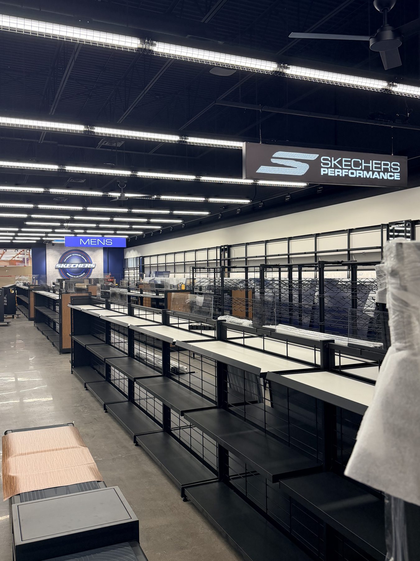 Empty store shelves with a "Mens" sign and branding overhead — Skechers (Signal Hill)