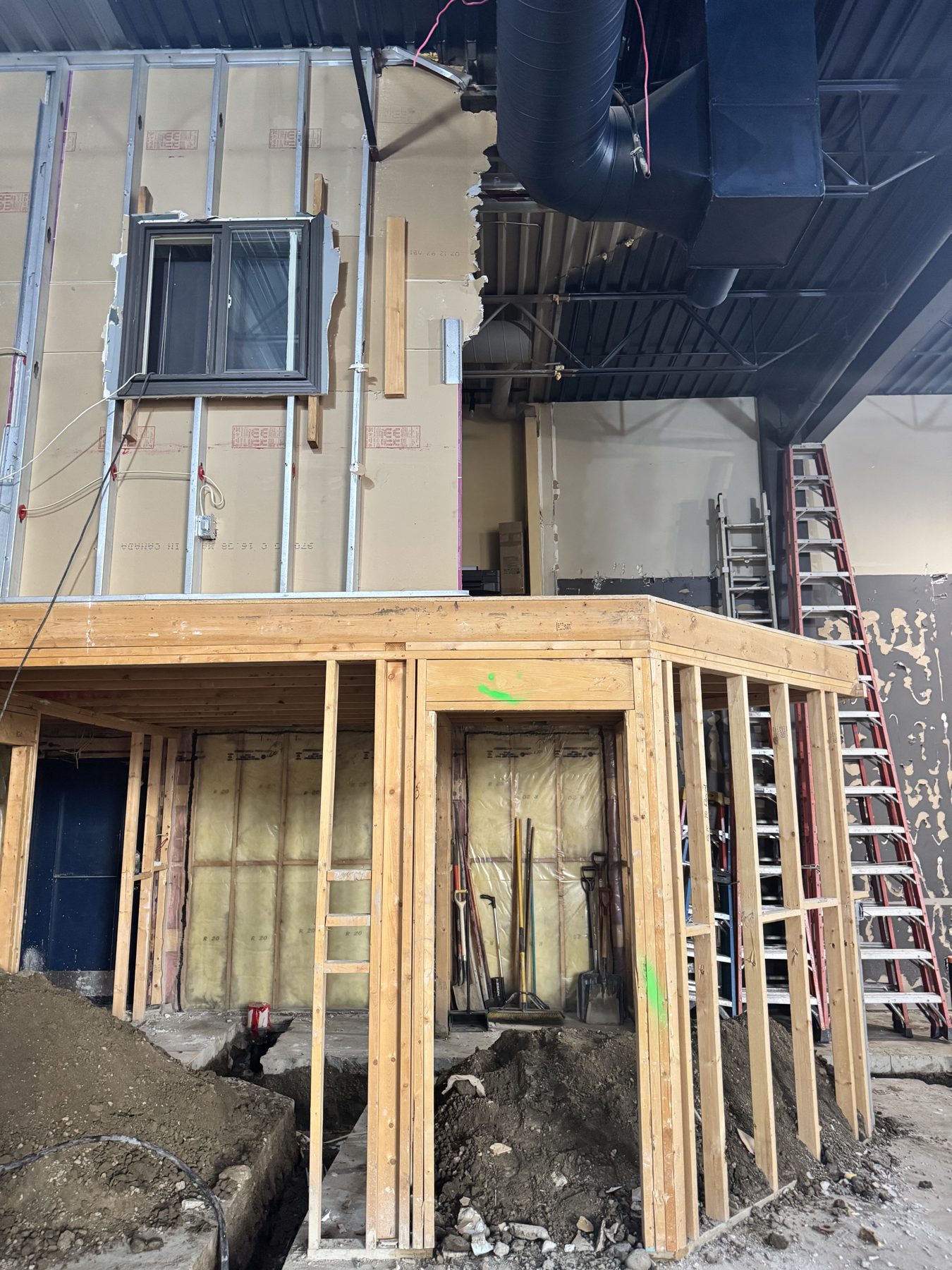 Construction site with new wooden framing, exposed insulation, and ladders — Blowers and Grafton (Red Deer)